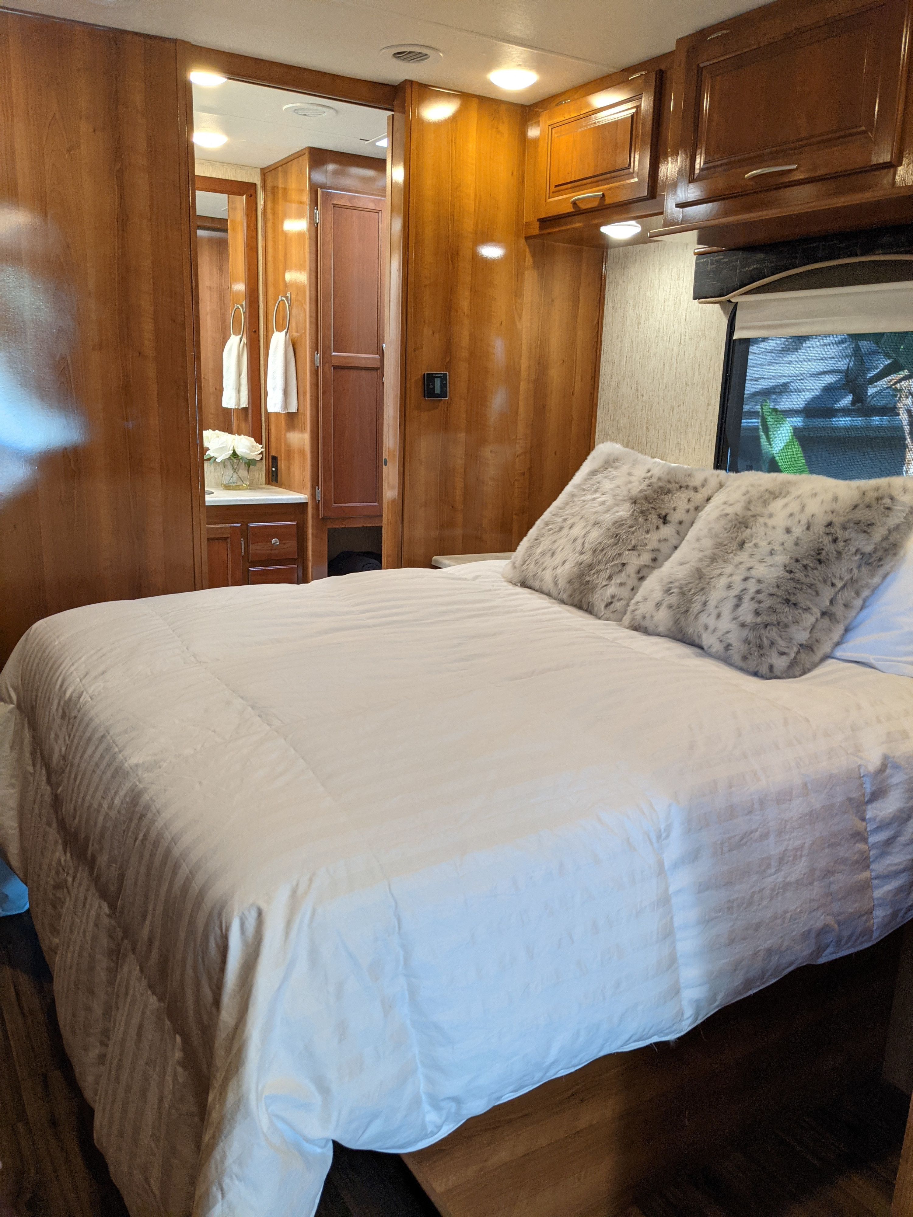 Cozy RV rental bedroom with plush white bedding, furry pillows, and warm wooden interior, offering a comfortable travel stay.. Coachmen Mirada 2019