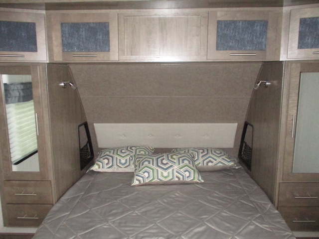 This RV rental bedroom features a cozy bed with pillows, overhead cabinets, and side wardrobes for storage.. Forest River Surveyor 2018