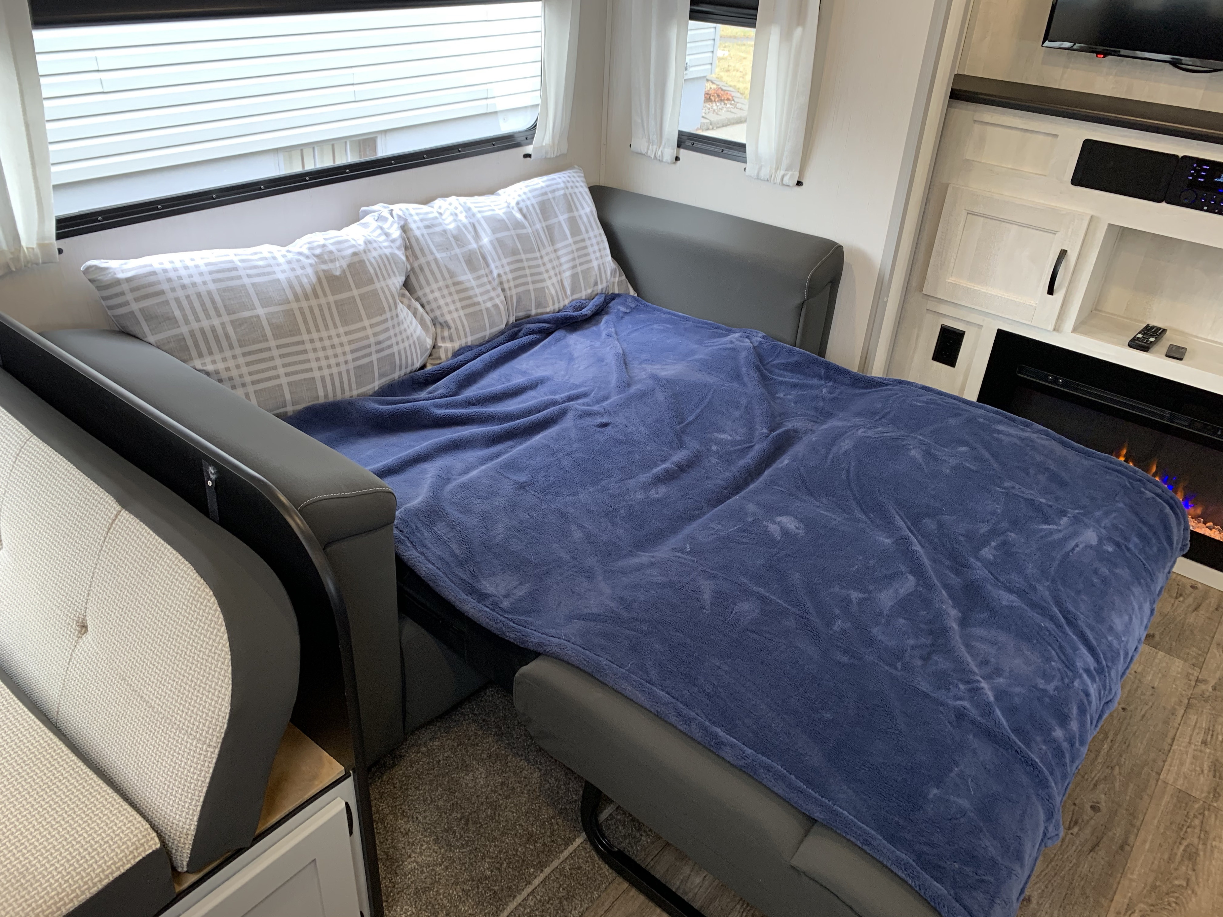 RV rental interior features a sofa bed pulled out, covered with a cozy blue blanket and plaid pillows, ideal for comfortable sleep.. Forest River Vibe 2021