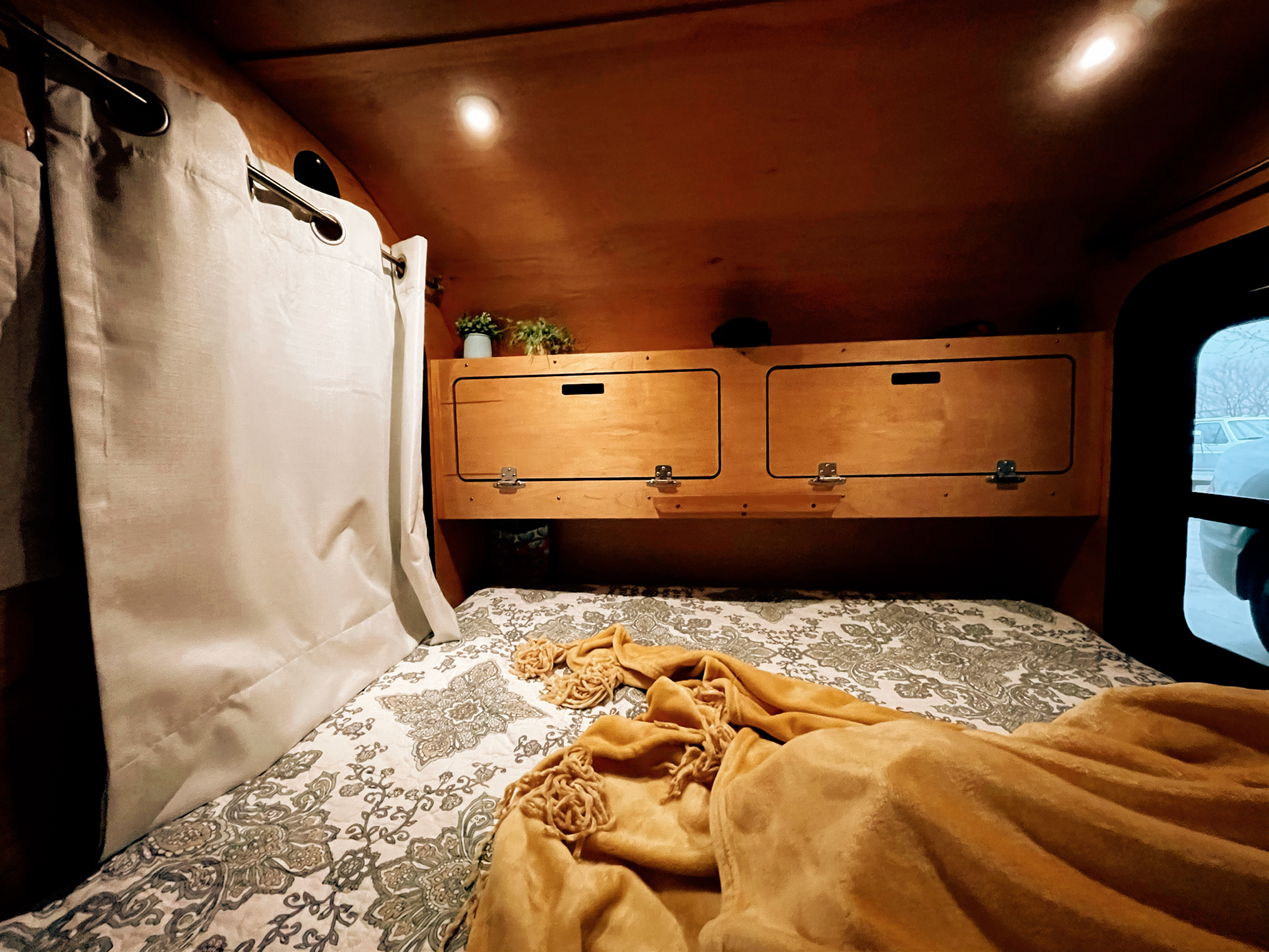 Cozy RV rental interior with a patterned bed, wood storage, bright lights, and window view, ideal for travel.. American Teardrop Travel Trailer 2016