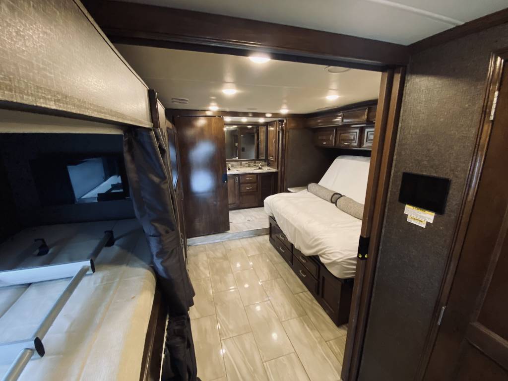 Modern RV rental interior showing bunk beds, master bedroom, and partial bathroom vanity. Spacious and comfortable layout.. Thor Motor Coach Aria 2018