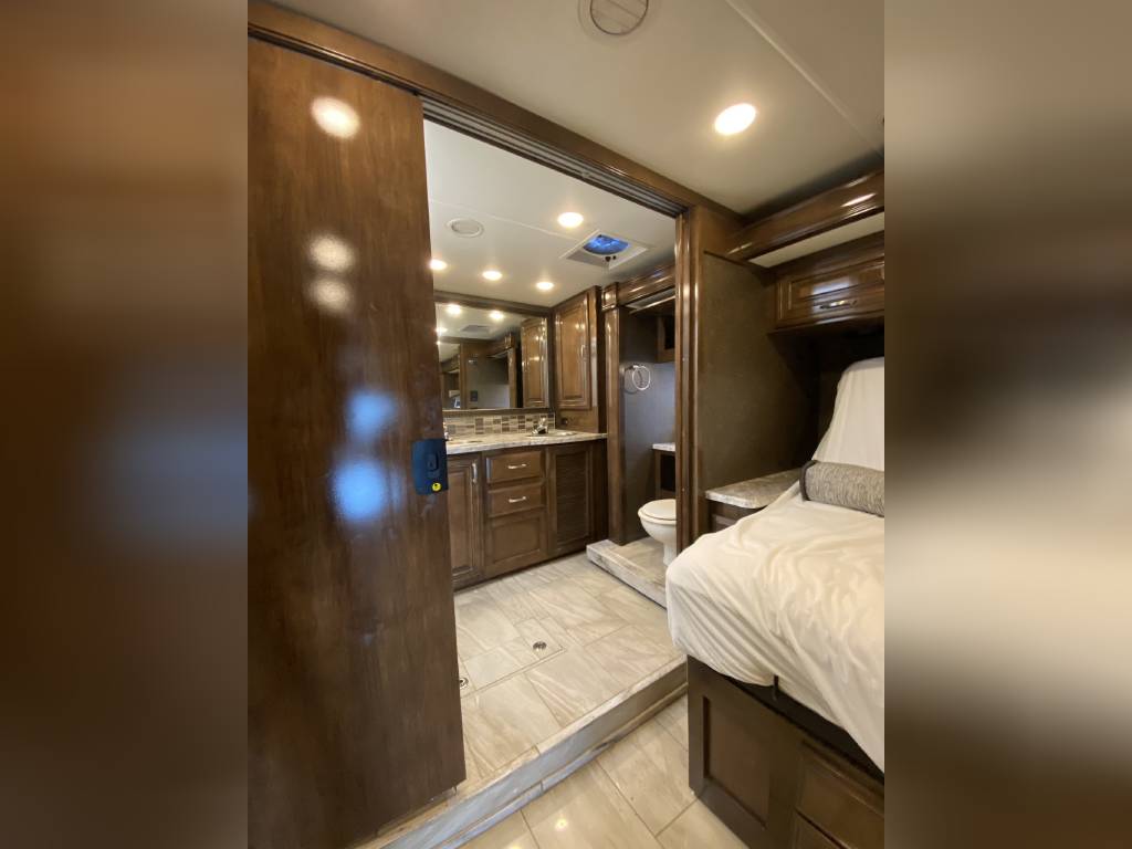 Inside an RV rental: a cozy bedroom with an open sliding door leading to a well-appointed bathroom with vanity and sink.. Thor Motor Coach Aria 2018