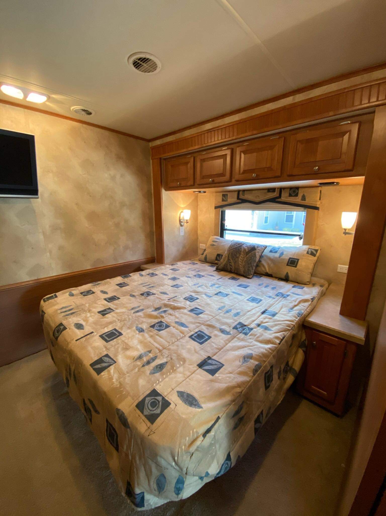 Step inside this inviting RV rental bedroom featuring a large bed, wooden cabinets, TV, and window. Ideal for comfortable journeys.. Allegro Allegro Motorhome 2009