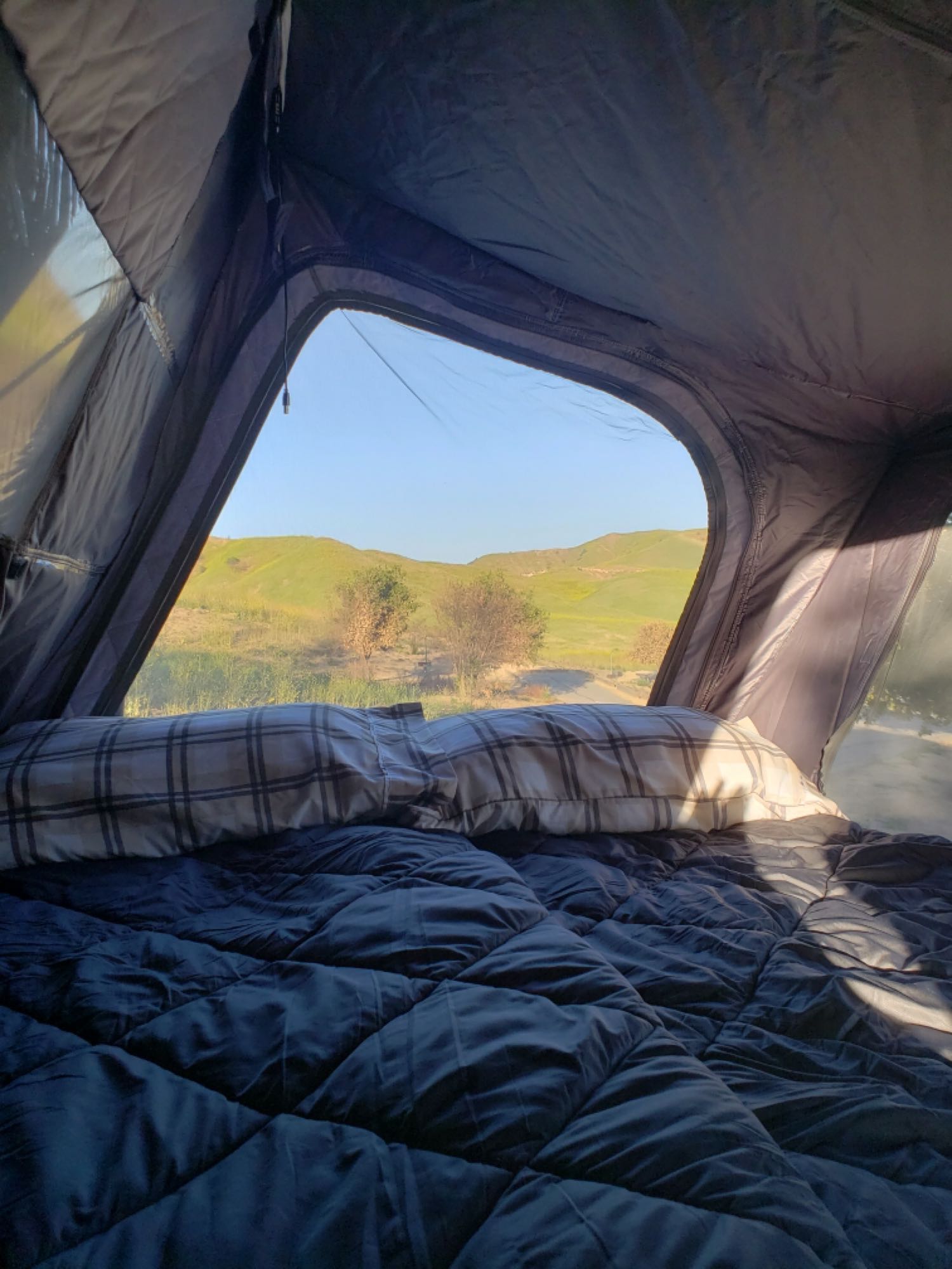 Comfortable bed in an RV rental, offering a scenic view of green hills under a blue sky. Perfect for outdoor adventures.. Other Other 2019