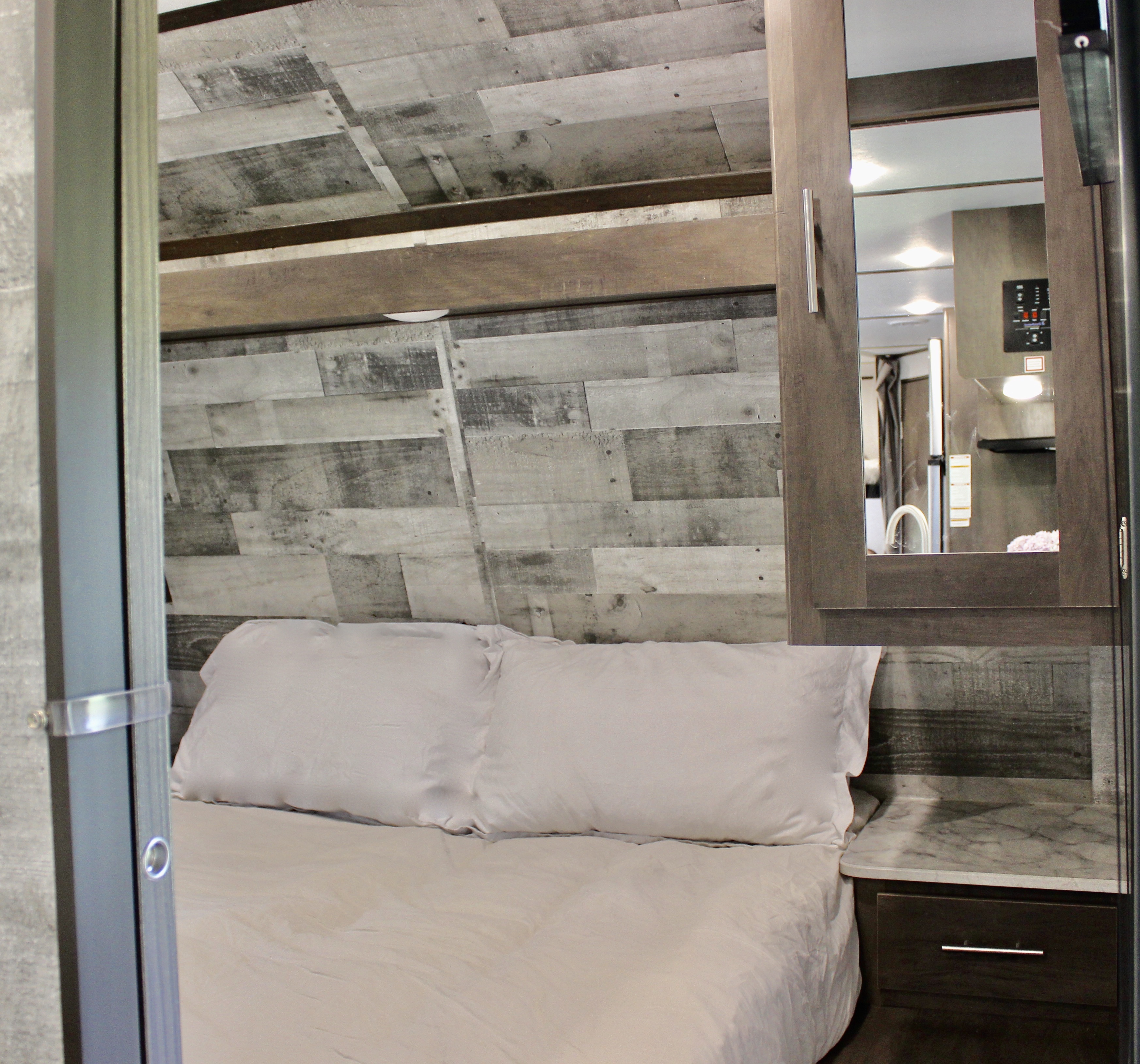 Comfortable RV rental bedroom featuring rustic wood walls, a cozy bed, and mirrored storage. Ideal for travel.. Dutchmen Coleman 2021