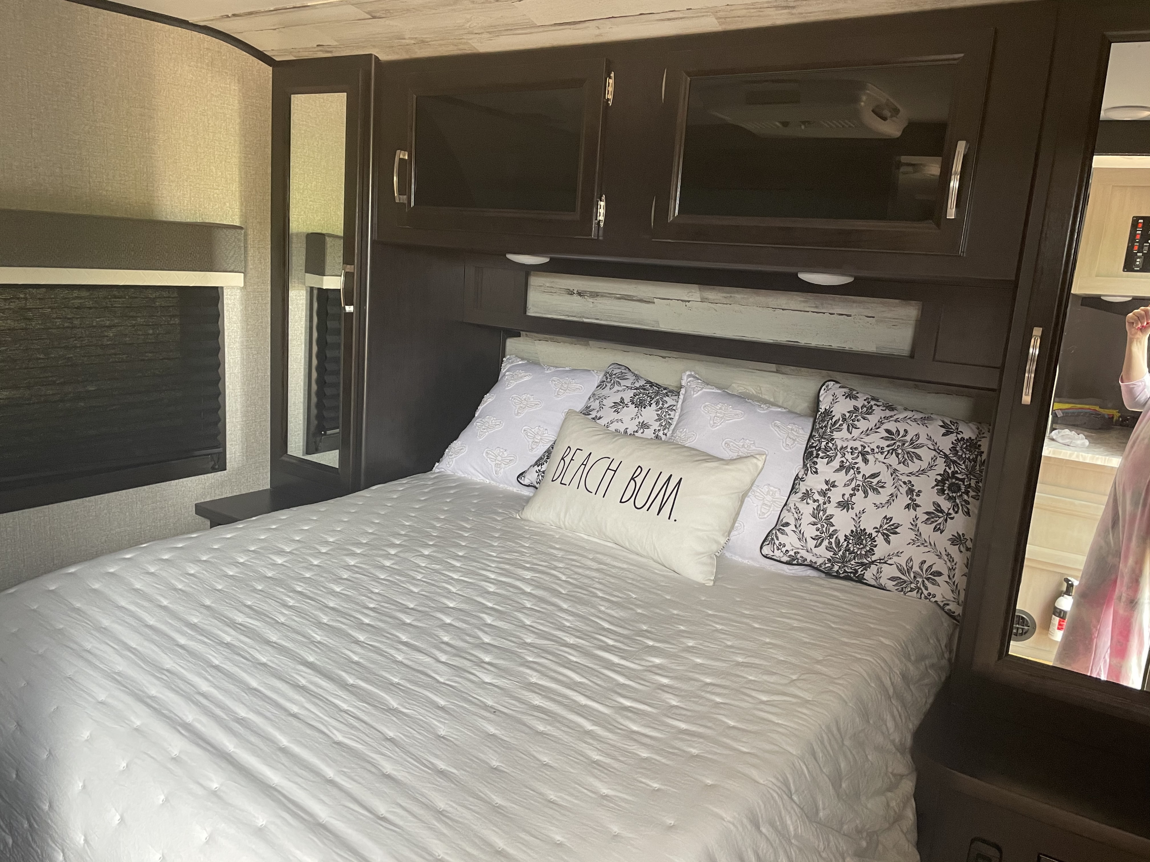 Relaxing RV rental bedroom showing a bed with white quilt, patterned pillows & dark wood cabinetry.. Jayco Jay Feather 2021