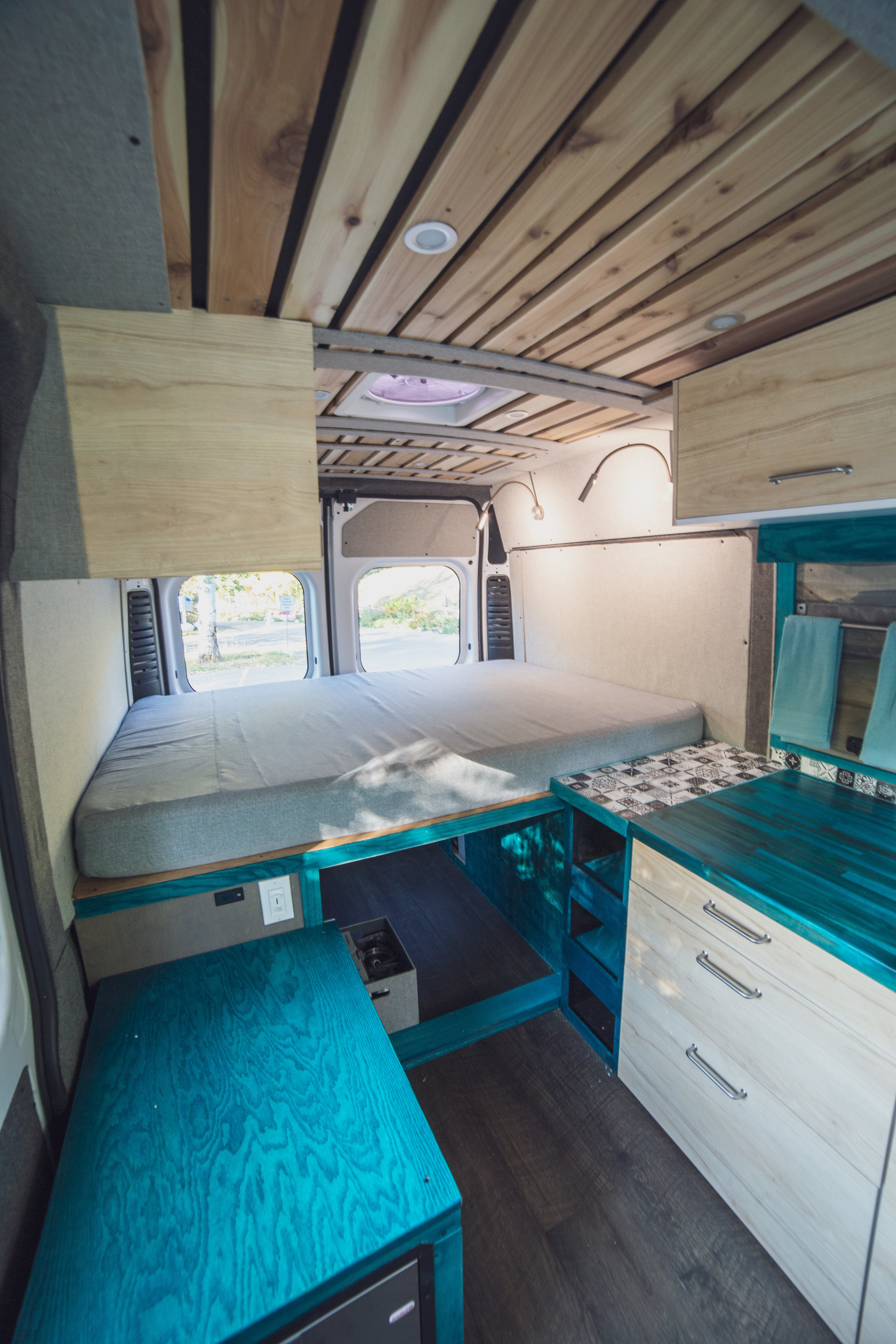 Bright RV rental interior with a comfy bed, unique teal kitchen counter, and slatted wood ceiling. A functional and stylish camper.. Dodge Ram 1500 2019