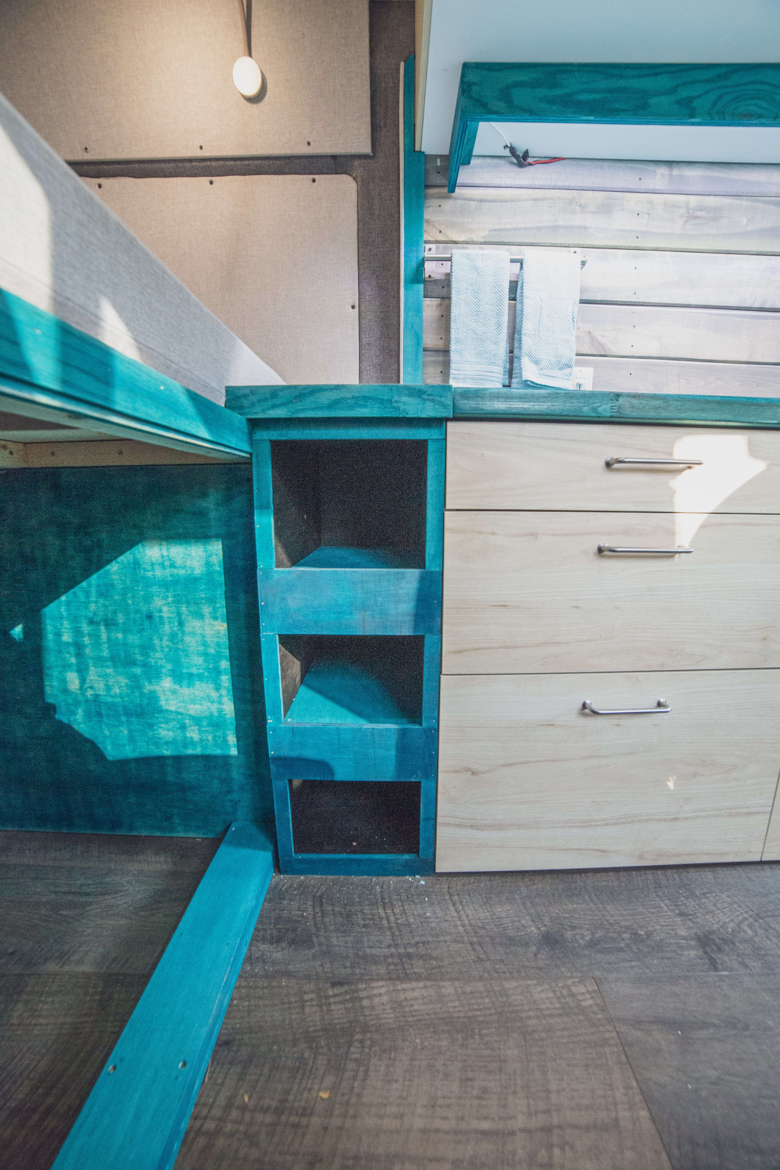 Compact RV rental interior featuring a turquoise bed frame, shelving, and wood drawers for smart storage.. Dodge Ram 1500 2019