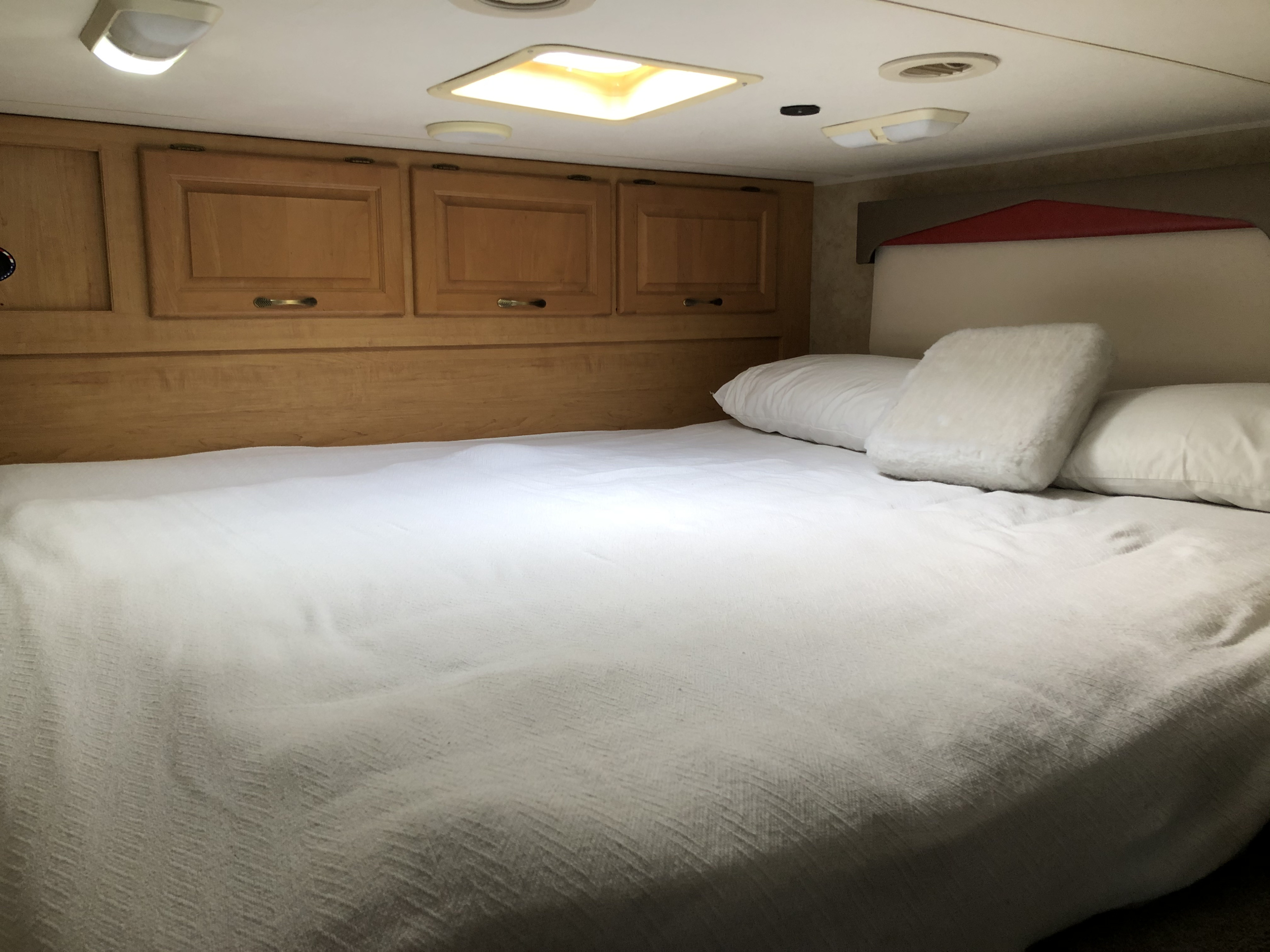 Bright RV rental bedroom featuring a plush white bed, pillows, and functional wooden storage cabinets above.. Damon Outlaw 2007