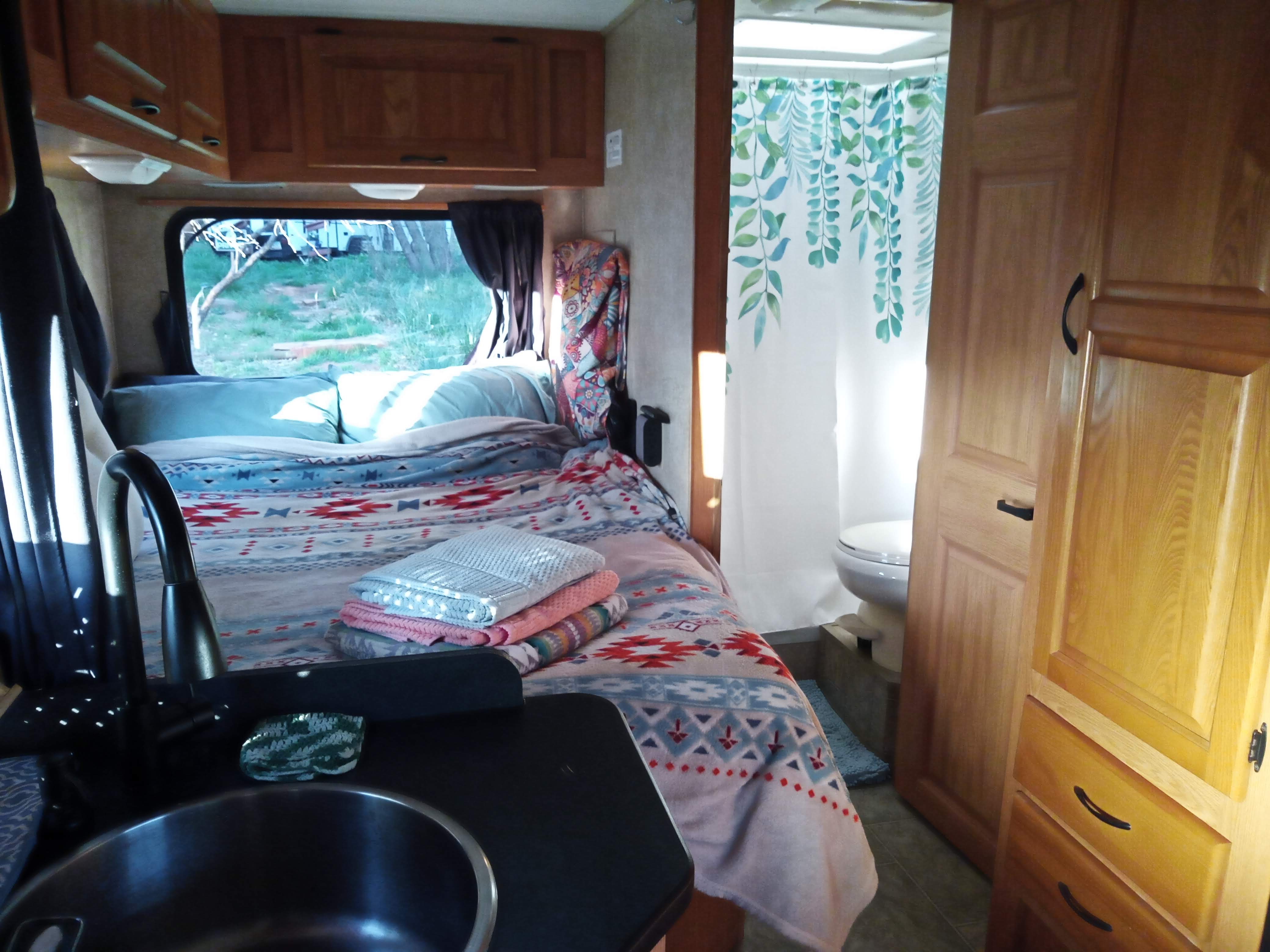 Cozy RV rental interior featuring a comfy bed with patterned blankets, a kitchen sink, and a compact bathroom.. Four Winds Majestic 2009