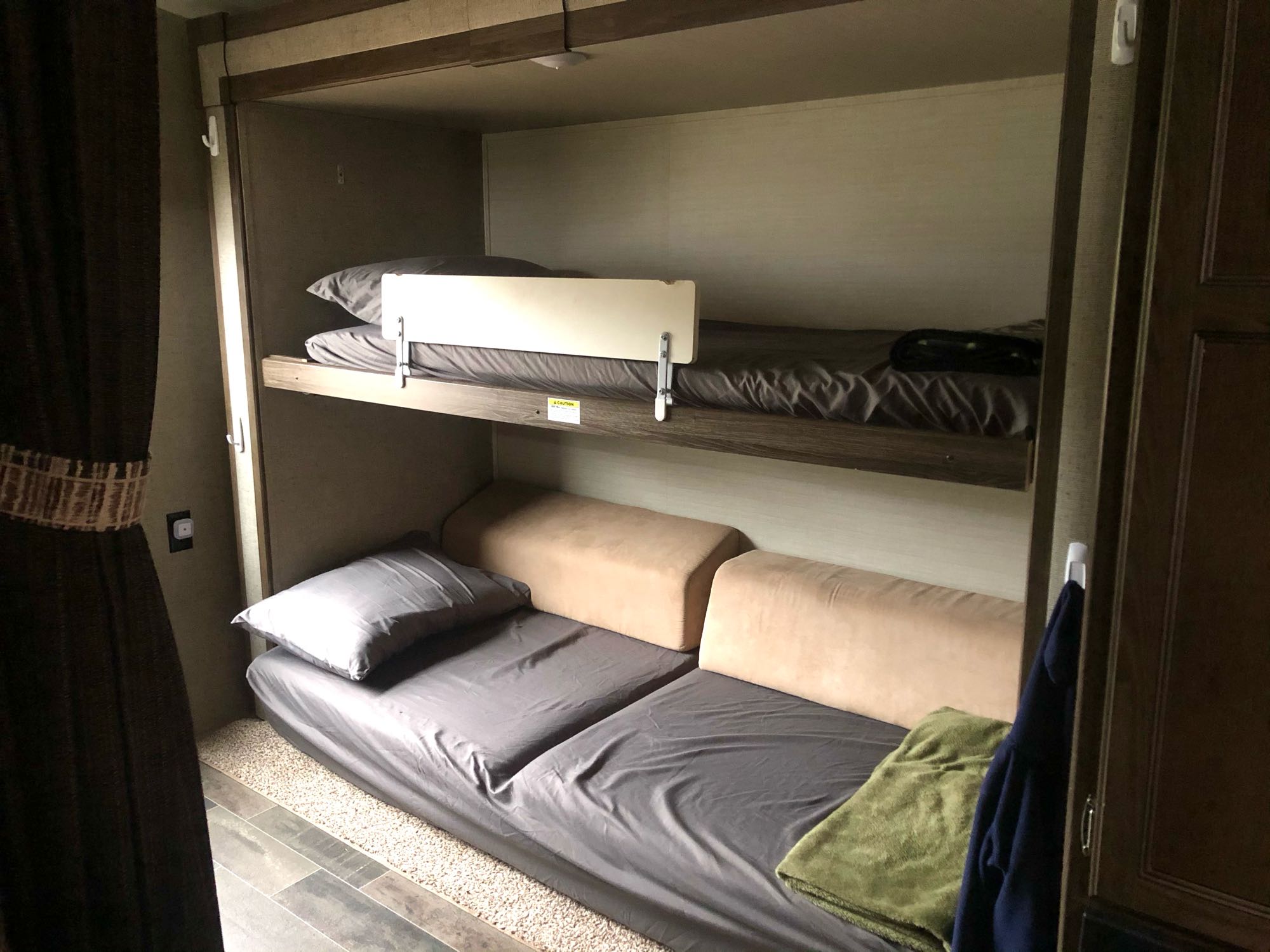 Cozy sleeping quarters in an RV rental featuring two bunk beds with a safety rail, and a lower bed/seating area with bedding.. Keystone Bullet Premier 2018