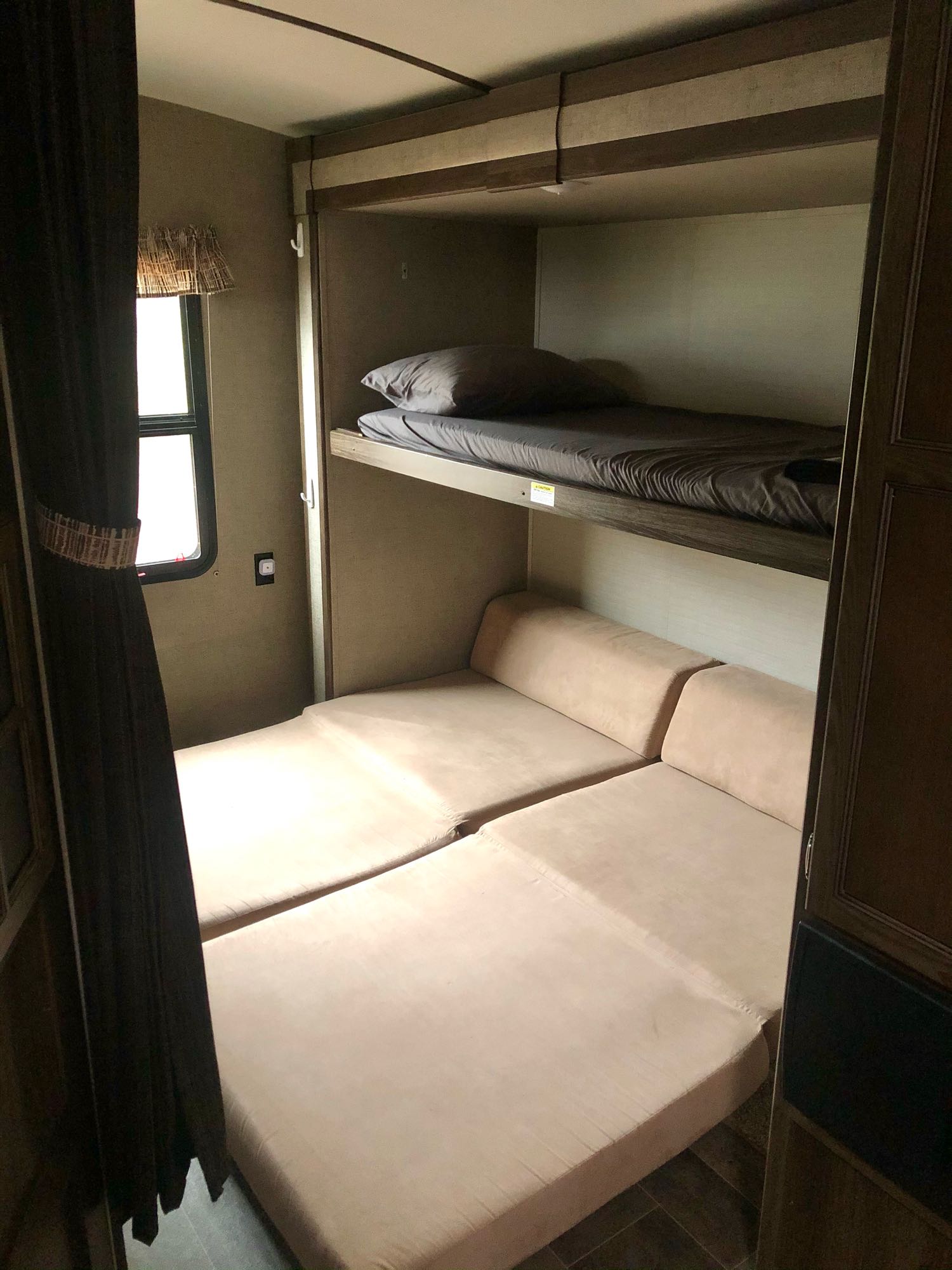Cozy RV rental interior with bunk beds above a tan convertible seating/sleeping area next to a window.. Keystone Bullet Premier 2018