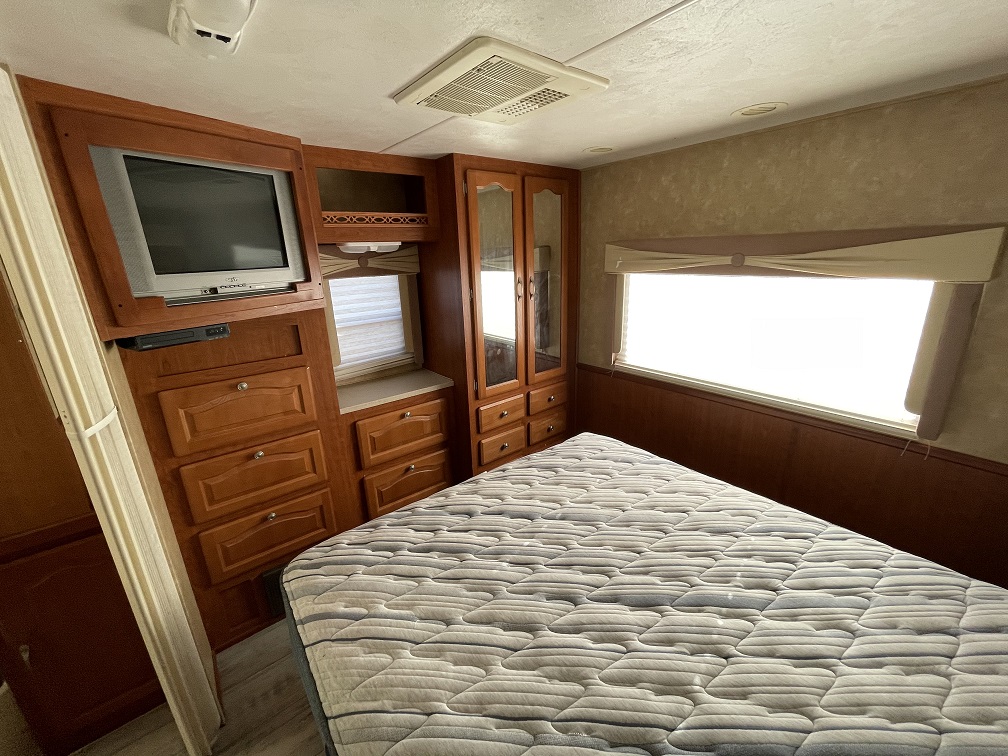 Experience a cozy RV rental bedroom featuring a comfortable bed, wood cabinetry, built-in TV, and bright windows.. Forest River Georgetown 2007