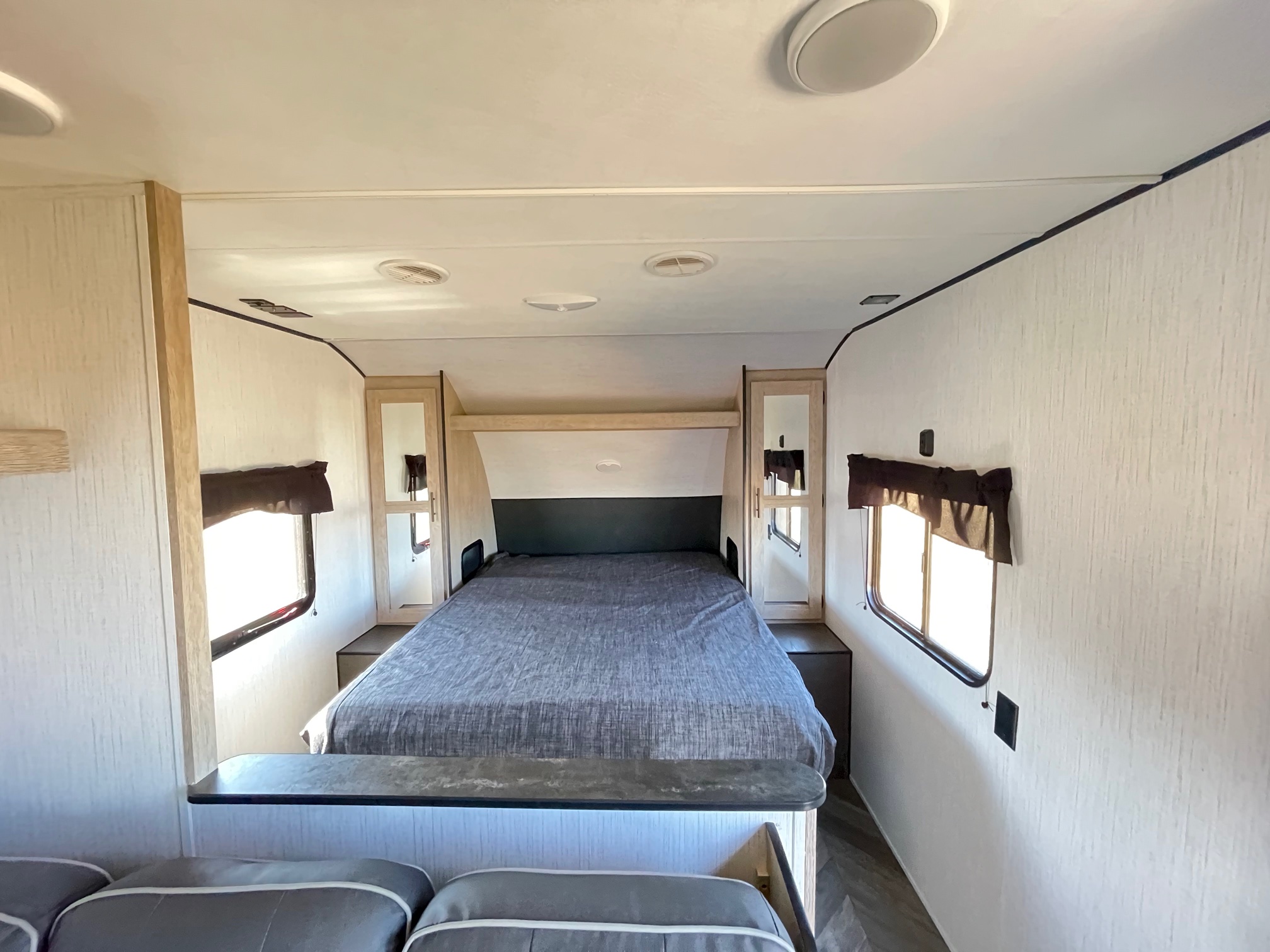 RV rental bedroom showing a large bed, side windows, overhead cabinets, and ceiling vents/lights. Perfect for your next trip.. Heartland Prowler 2021