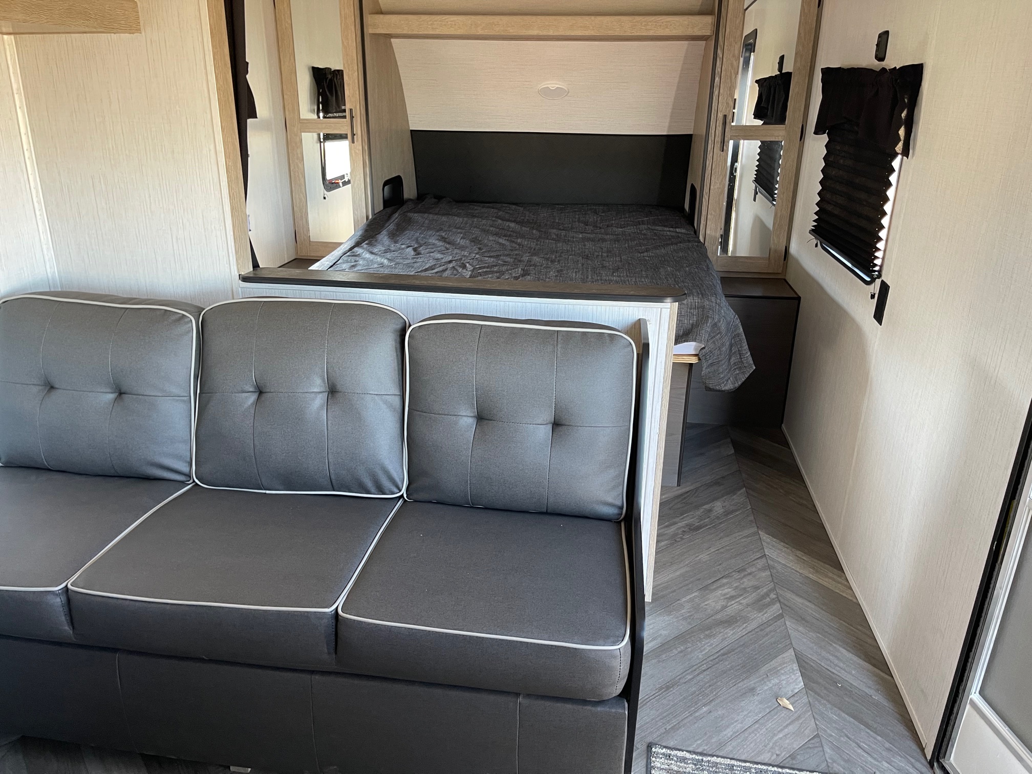 Inside an RV rental: a modern gray sofa and a full-size bed offer compact comfort. Ideal for travel.. Heartland Prowler 2021