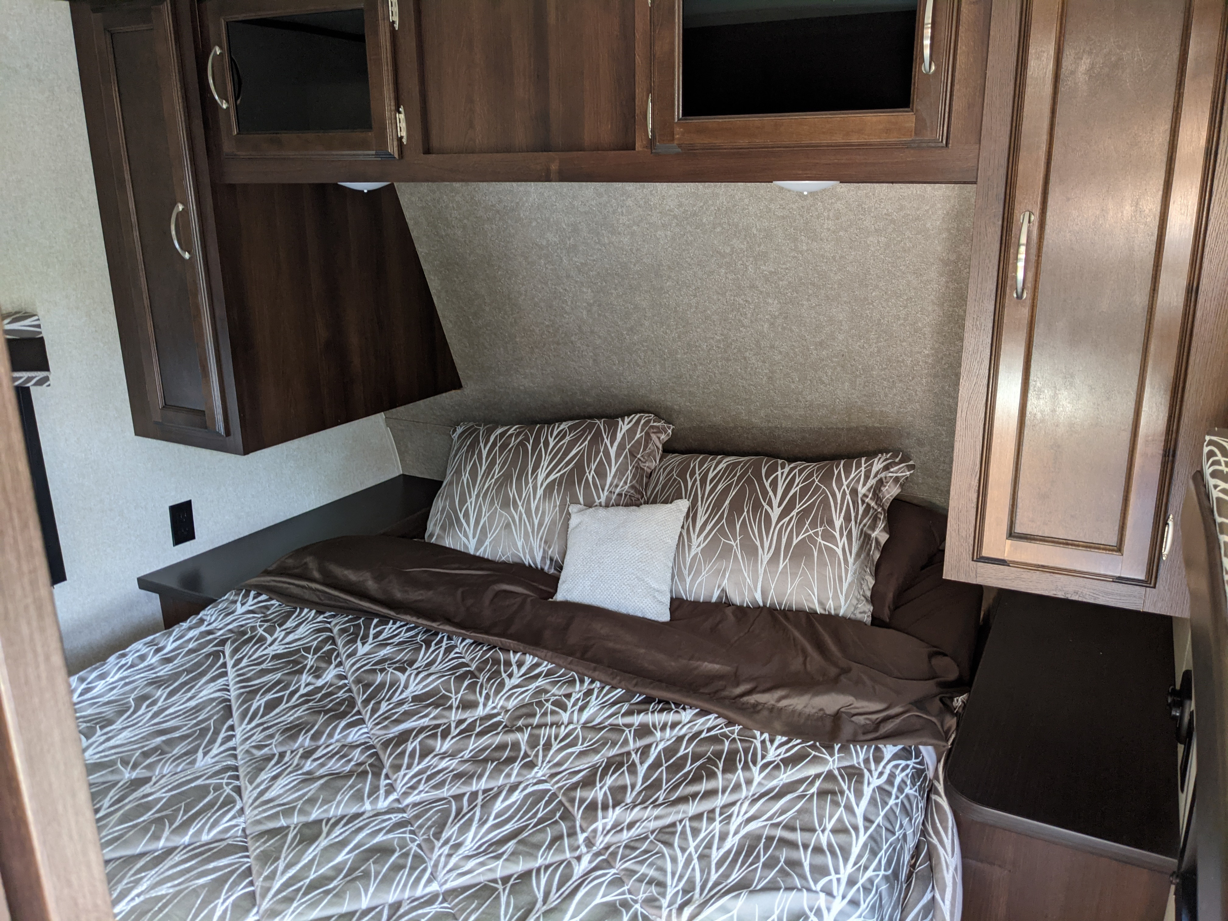 RV rental bedroom featuring a bed with brown & white tree-patterned bedding, dark wood cabinets, and integrated nightstands.. Jayco Jay Flight 2018