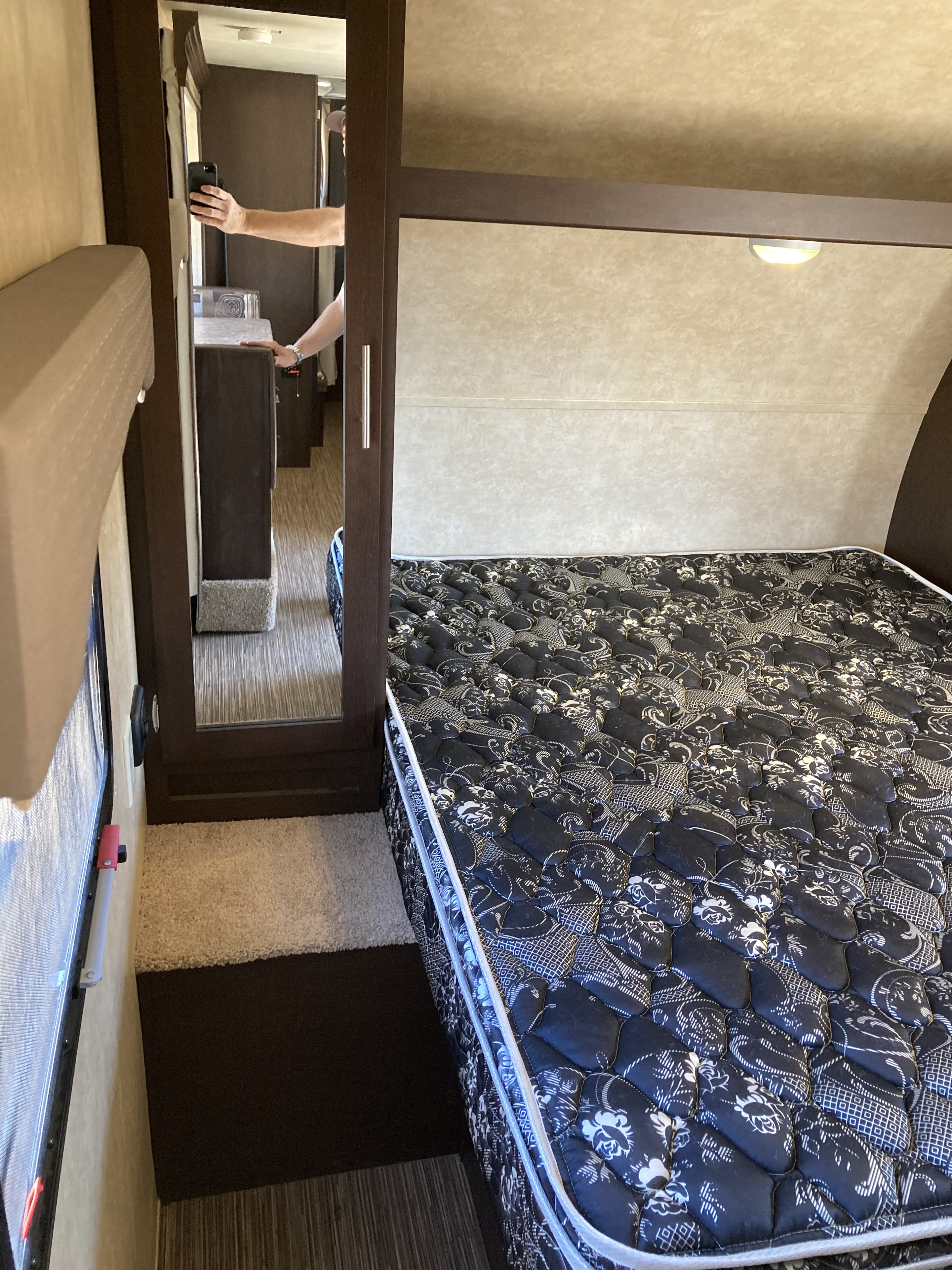 This RV rental shows a compact bedroom featuring a black patterned mattress. A mirror reflects the photographer, offering a glimpse of the RV's interior.. Forest River Evo 2016