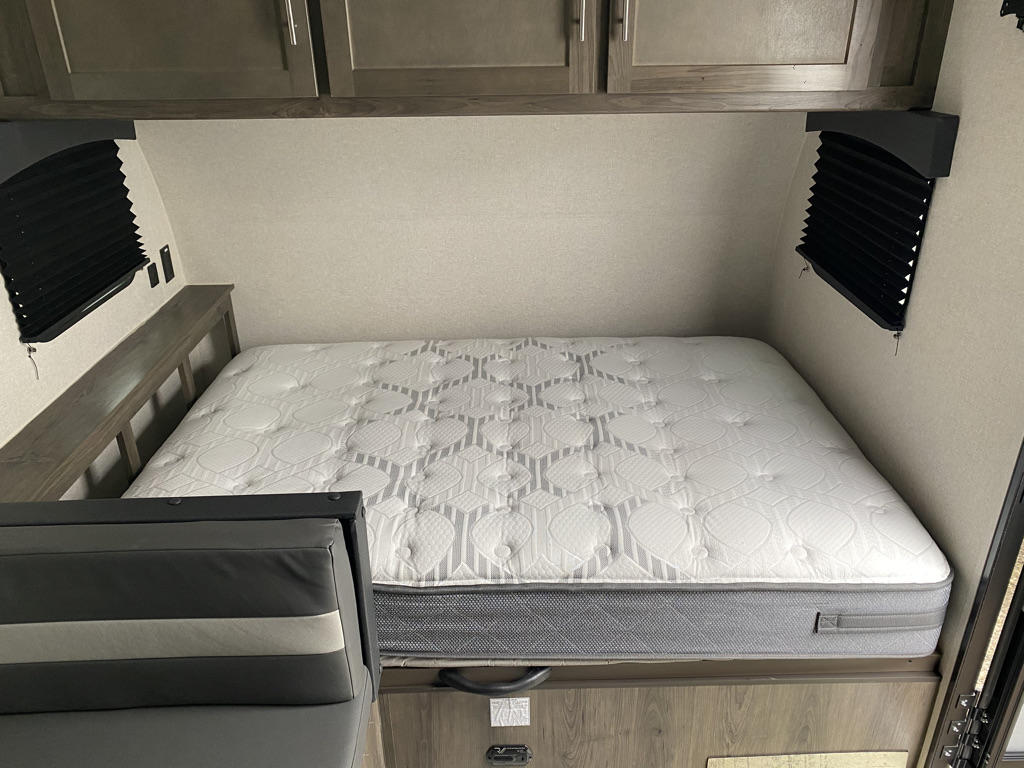Cozy sleeping area in an RV rental, featuring a white patterned mattress, side windows, and convenient overhead storage.. Viking 17BH 2021