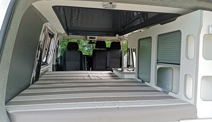 Cozy RV rental camper van interior with a bed, kitchen hob, and storage, designed for comfortable road trip adventures.. Volkswagen Transporter T6 2021