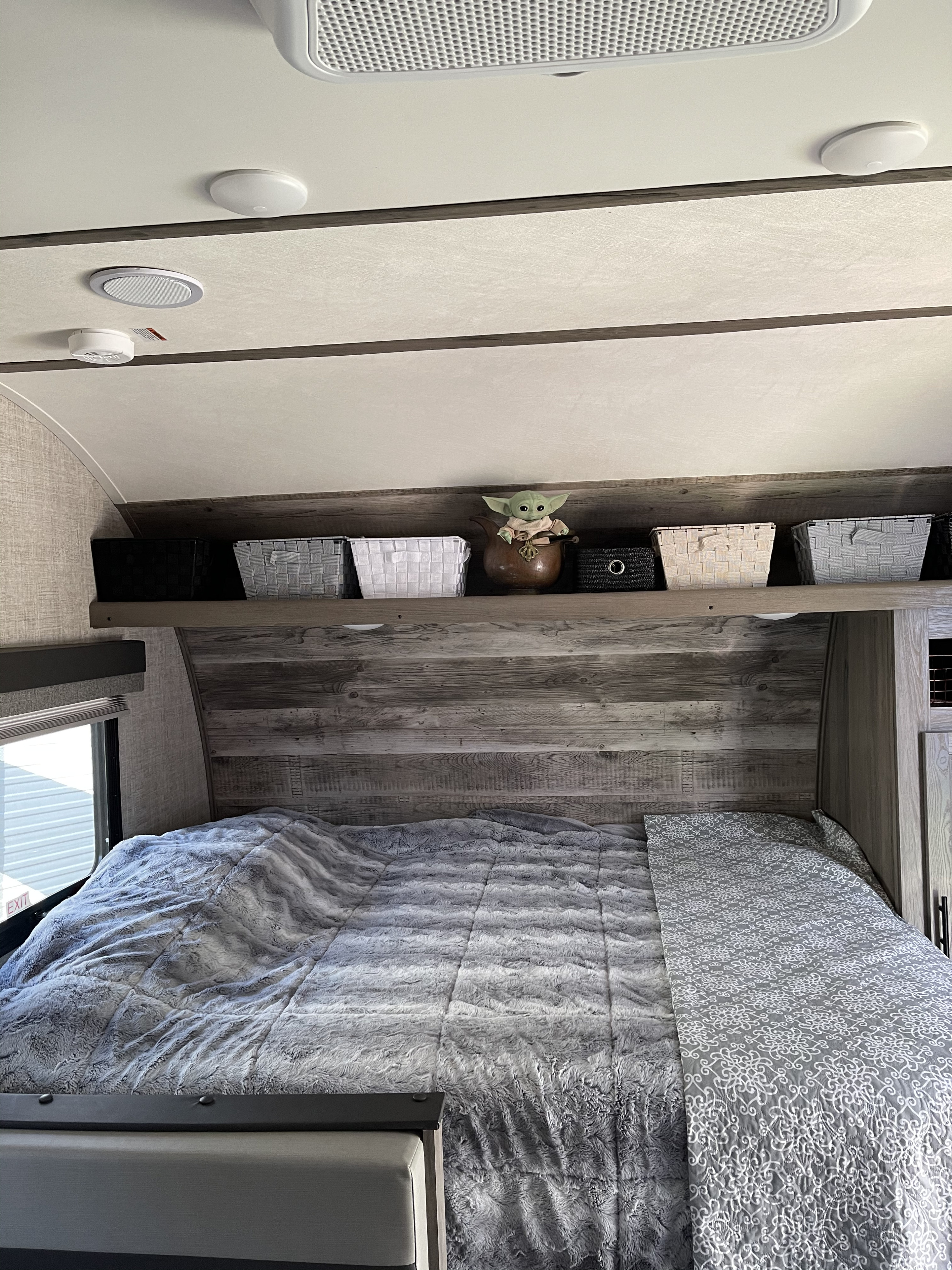 Relaxing RV rental bedroom showing a plush bed, rustic wood headboard, and organized overhead storage with Grogu.. Gulf Stream Amerilite 2021