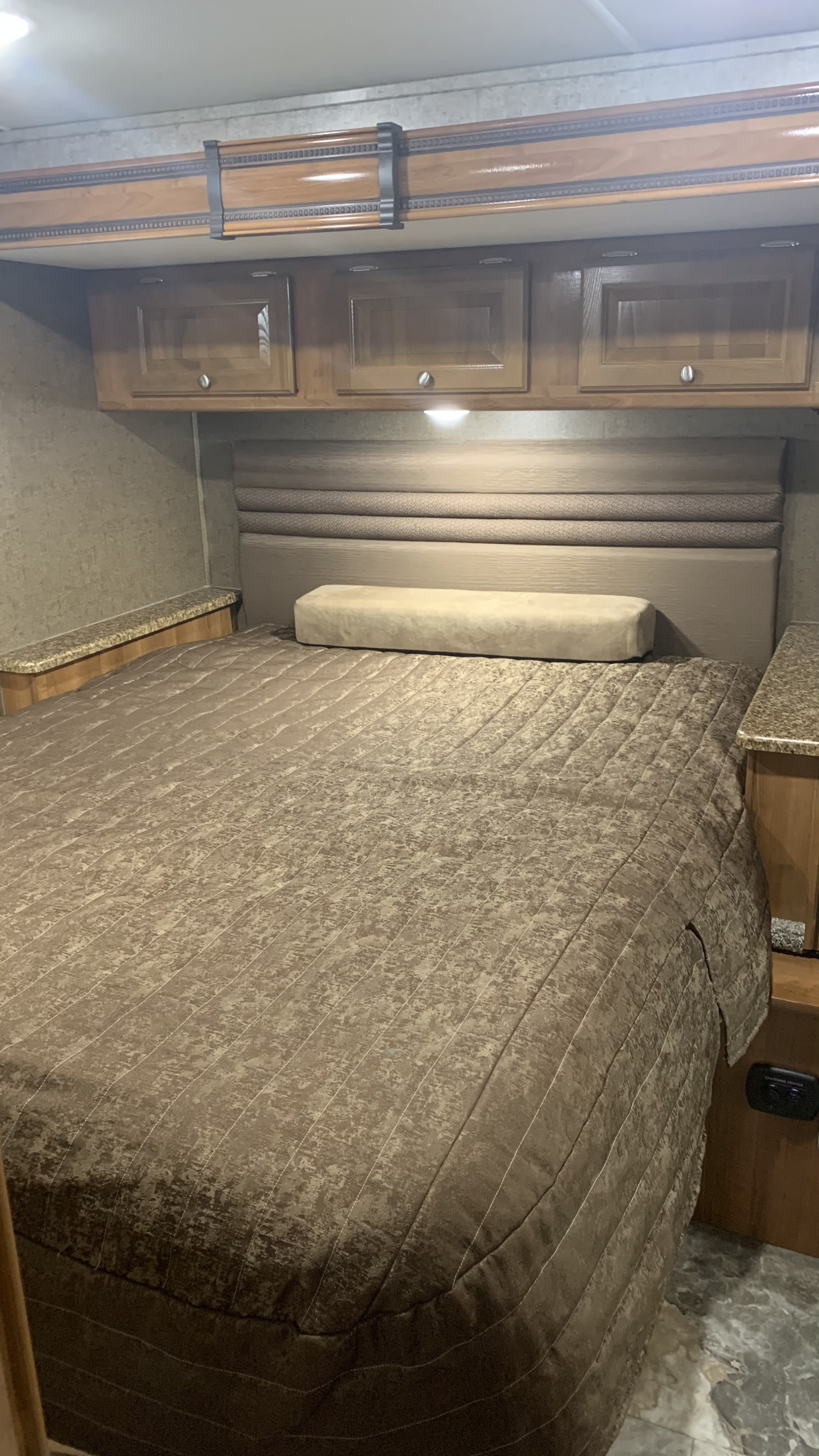 Cozy RV rental bedroom features a comfy bed, modern headboard, and overhead wood cabinets.. Other Other 2018