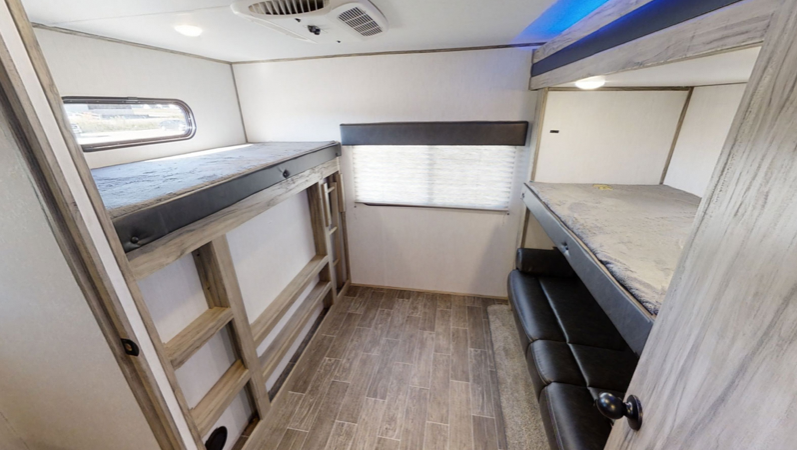 Spacious RV rental bunkhouse featuring two sets of bunk beds, one with a ladder, and a lower sofa bunk. Wood floor & window.. Forest River Alpha Wolf 2021