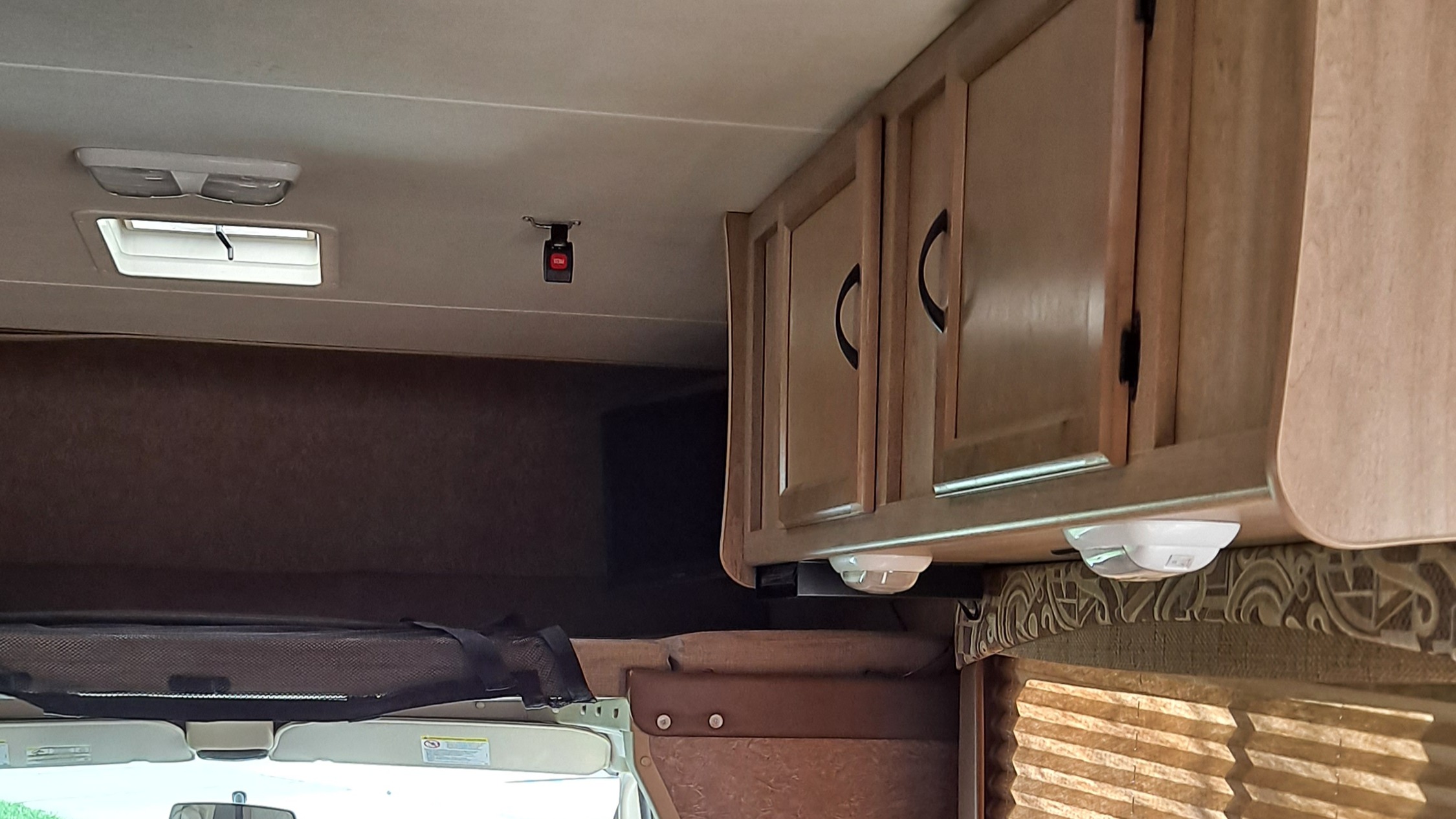 RV rental interior with over-cab bunk, safety net & buckle, overhead wood cabinets, and ceiling lights.. Coachmen Freelander 2015