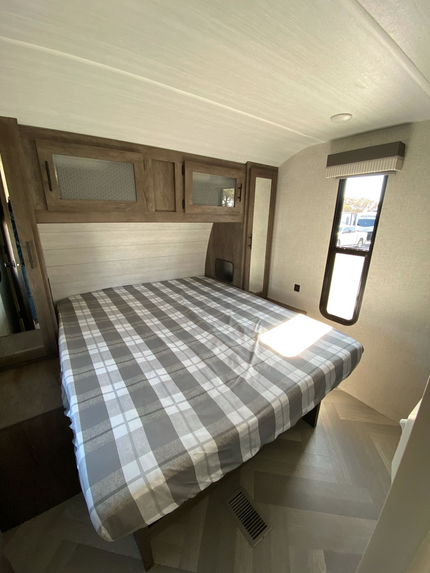 Spacious RV rental bedroom featuring a bed with plaid bedding, overhead cabinets, and a window for natural light. Ideal for travel.. Forest River Wildwood 2021