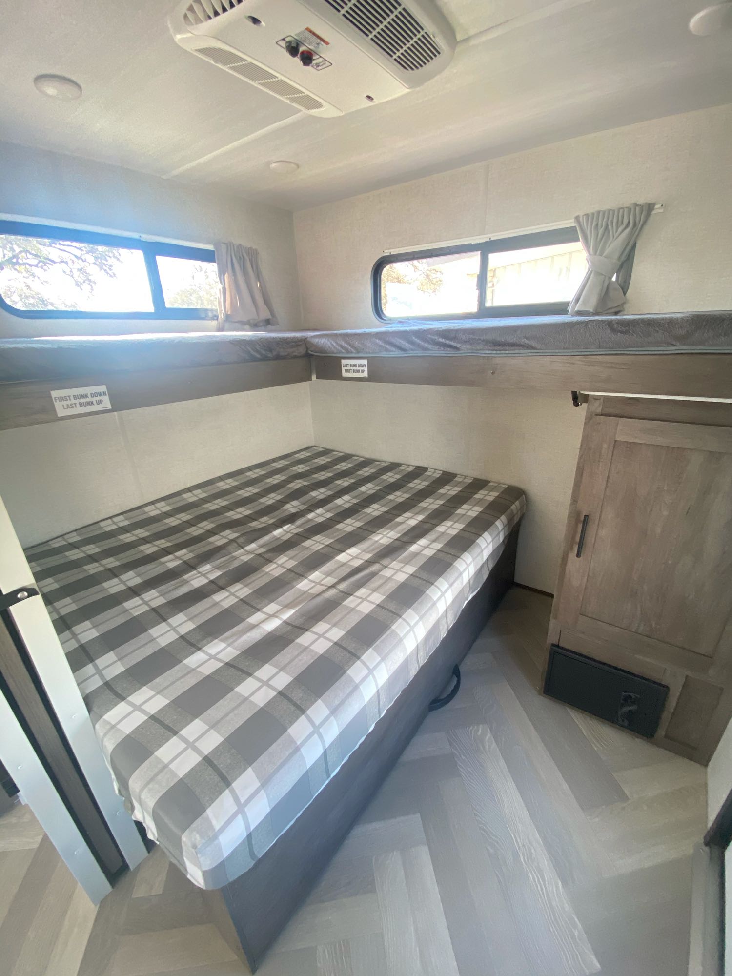 This RV rental offers a flexible bunk room with cozy plaid lower bed, upper bunk, AC, and light wood-look floor.. Forest River Wildwood 2021