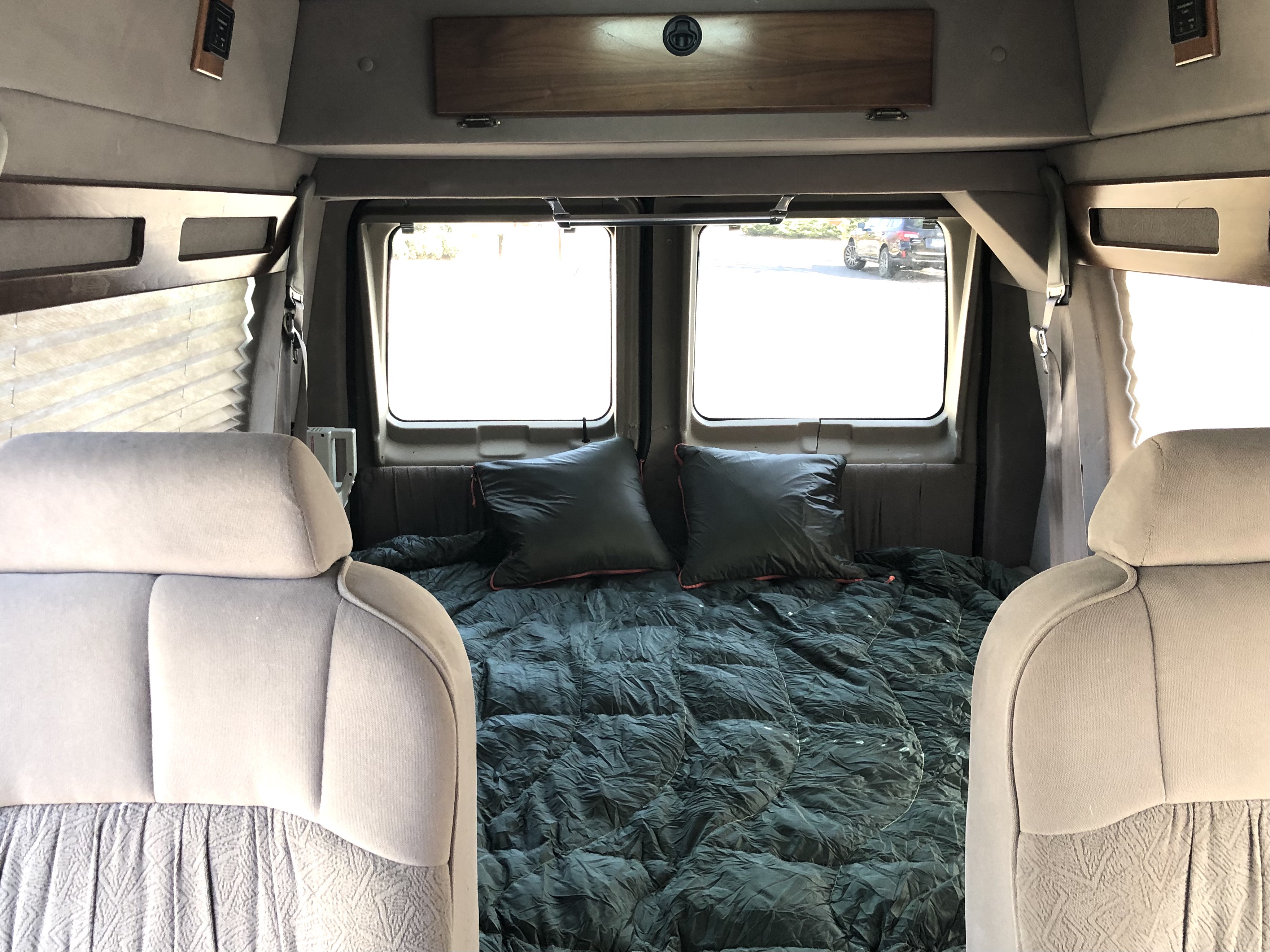 Step inside this cozy RV rental's camper van interior, featuring a comfortable bed, pillows, and bright windows for mobile travel.. Ford Econoline 1997