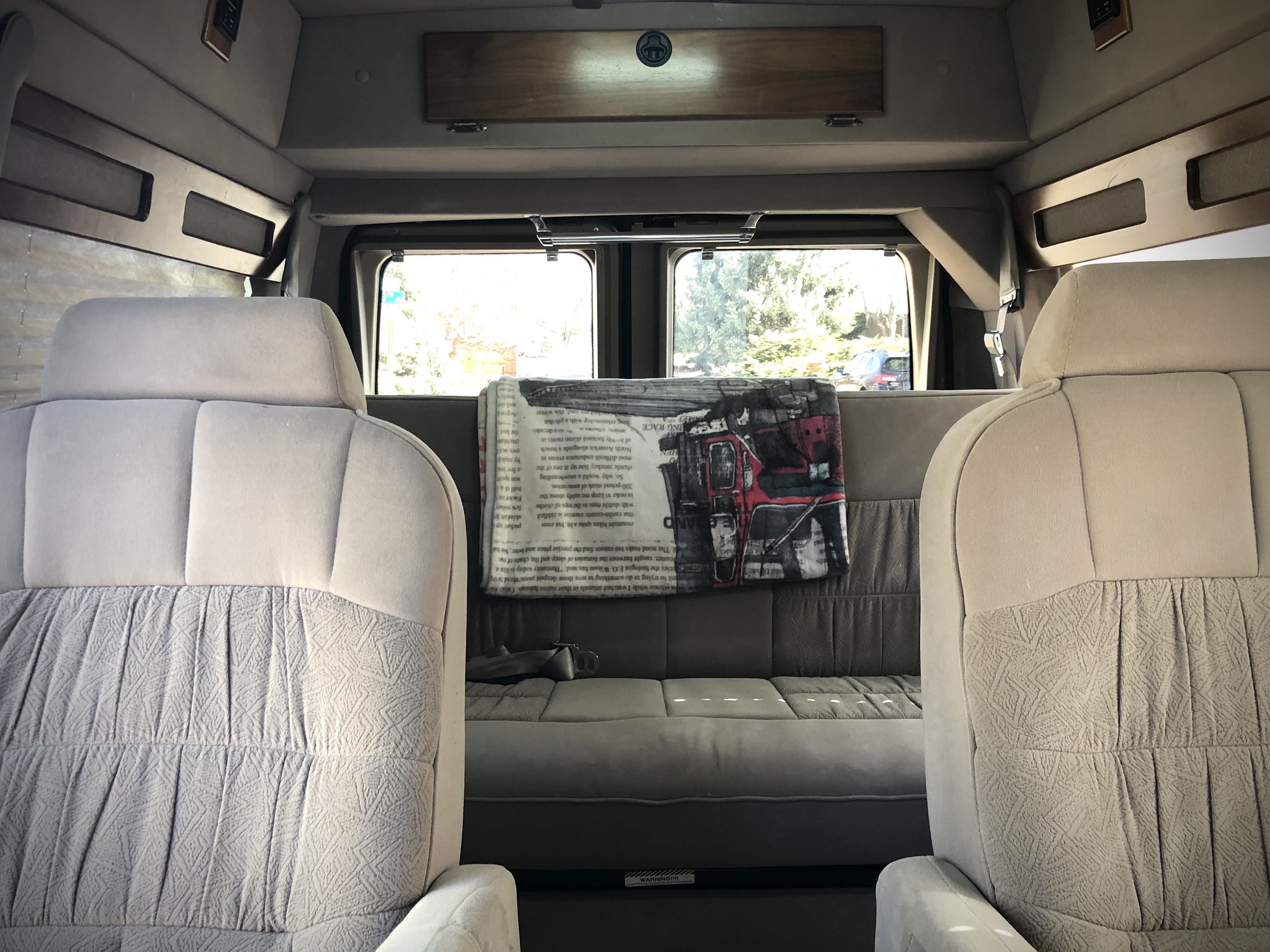 Comfortable RV rental van interior with light-colored front seats, a grey rear sofa, and large windows.. Ford Econoline 1997