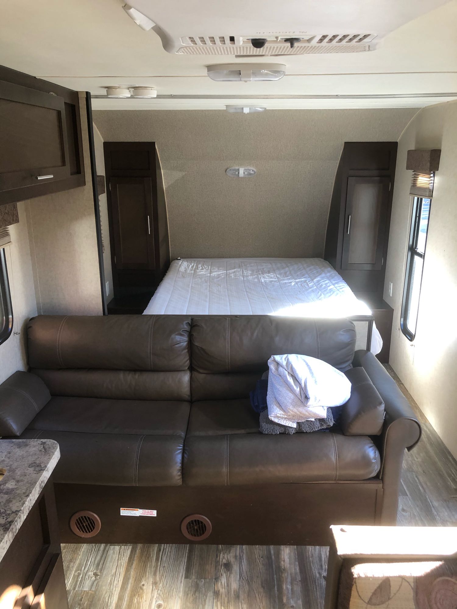 Interior of an RV rental: a spacious living area featuring a comfortable brown couch, leading to a queen-sized bed in the back.. Forest River Cherokee Grey Wolf 2016