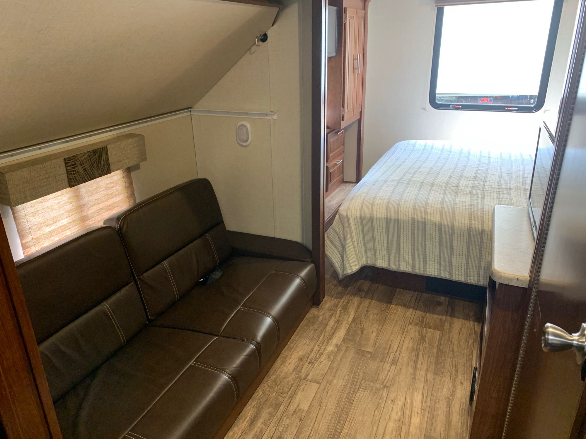 Inside an RV rental: a cozy space featuring a brown leather sofa, a bed with striped covers, and wood-look flooring.. Forest River Fr3 2017