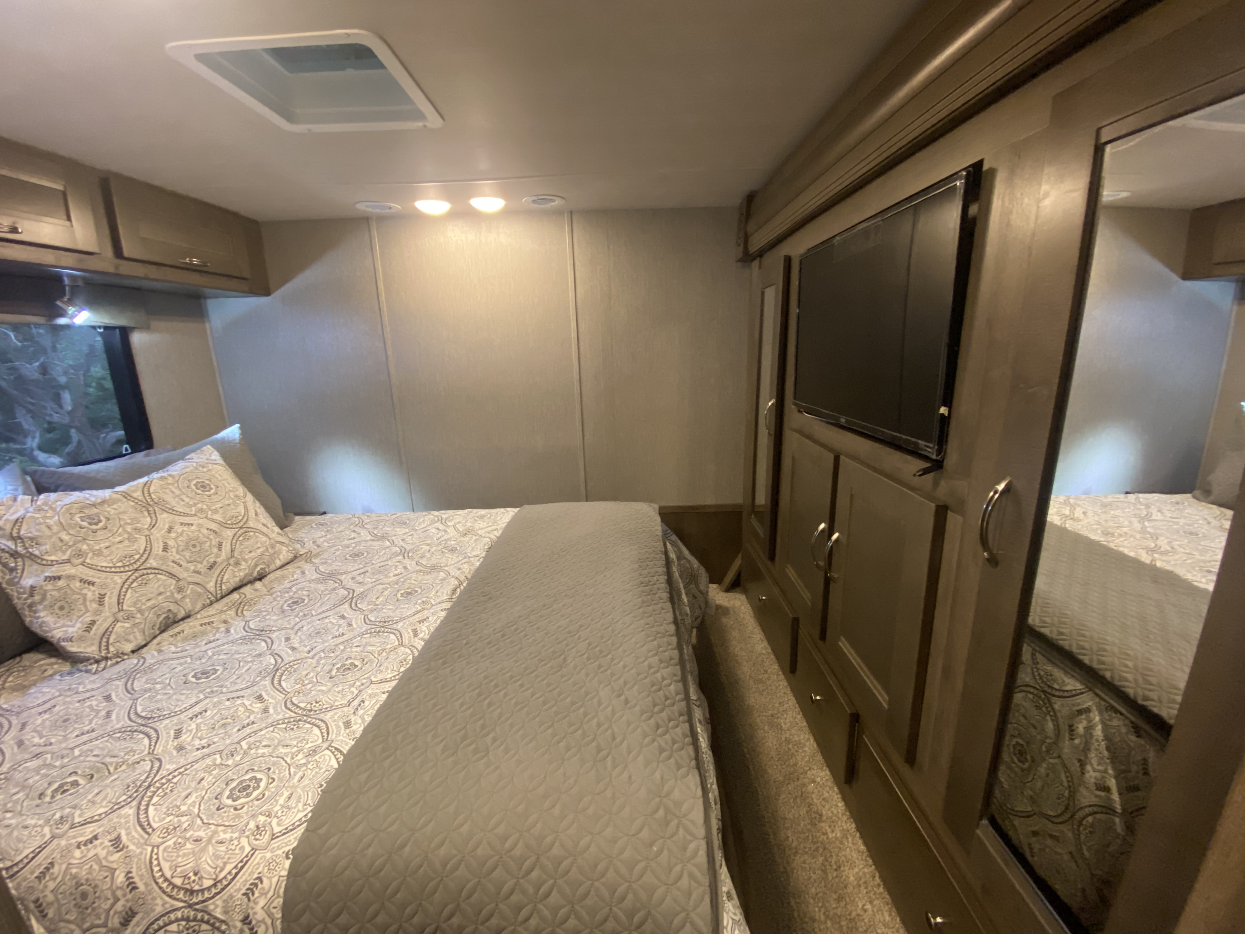 Inside this RV rental bedroom: a comfortable bed with patterned bedding, TV, and mirrored wardrobe for your trip.. Nexus Triumph 2021