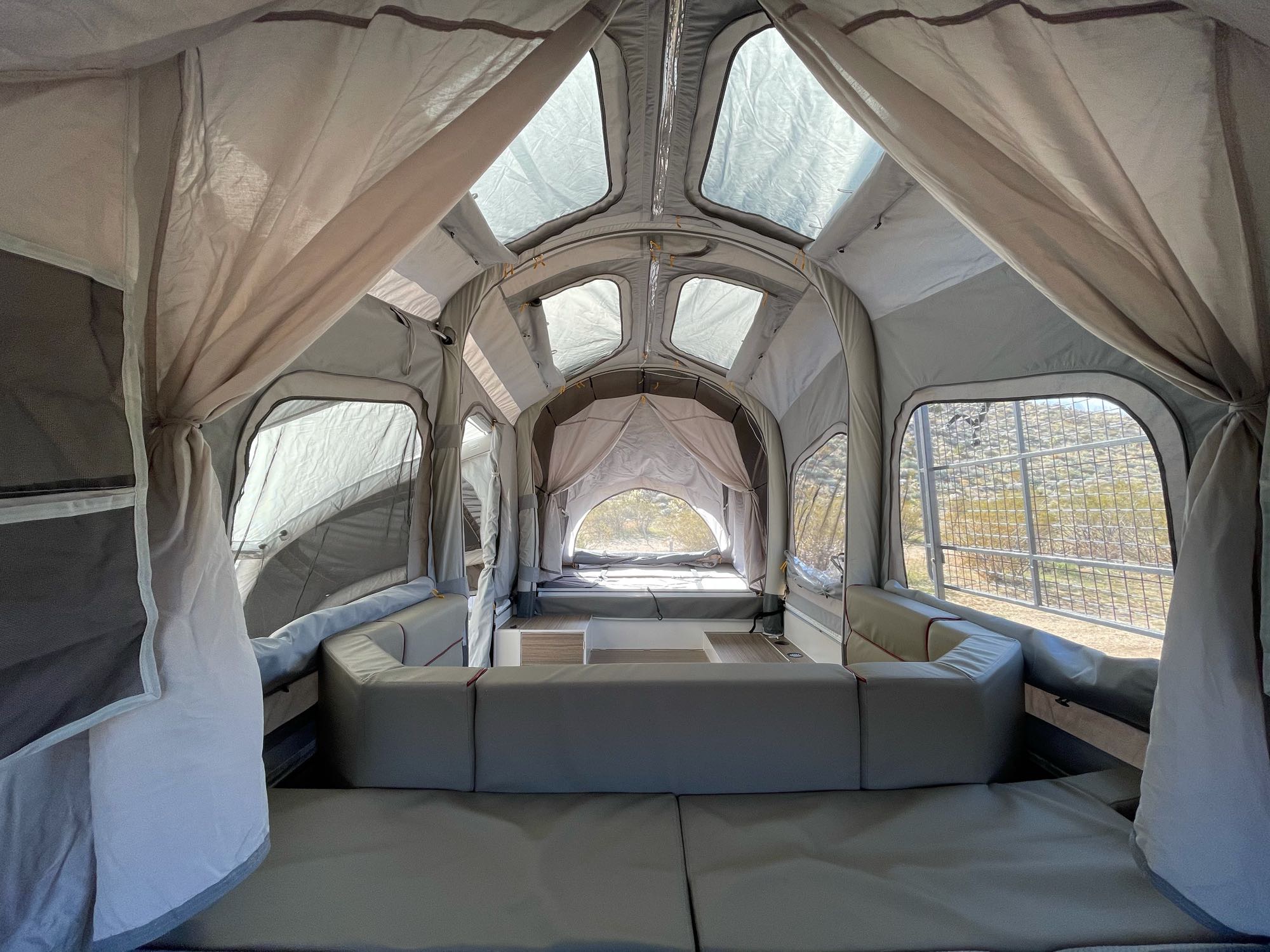 View inside a spacious RV rental. Grey fabric interior with modular seating/beds, clear roof, and outdoor views.. Opus OP4 Off Road 2020