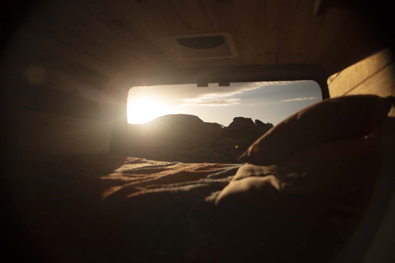 Wake up to desert views from your RV rental! Cozy bed inside, with sun over mountains through the window.. Ram Promaster 2021