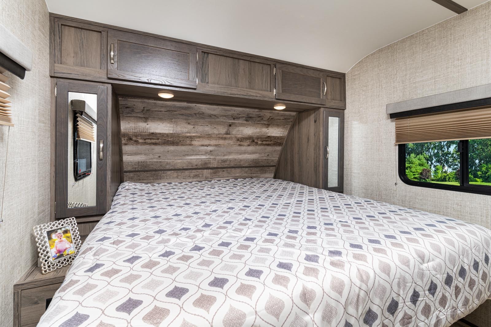 RV rental bedroom features comfy bed, wood-paneled headboard & overhead cabinets, plus a window with nature views.. Gulf Stream Envision 2021