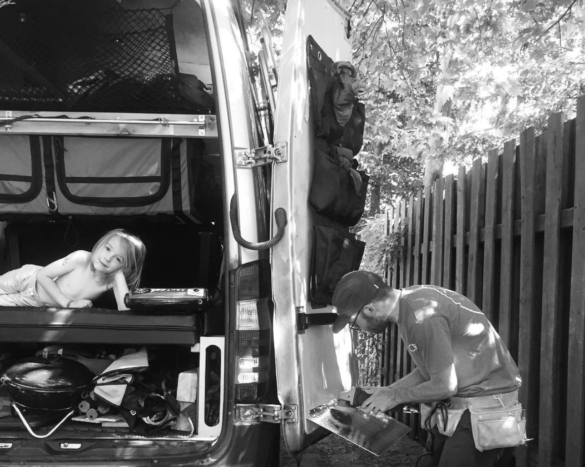 Enjoying an RV rental! A child lies inside the camper van, while a man in a tool belt works outside near a fence.. Mercedes-Benz Sprinter 4x4 315CDI MWB 2015