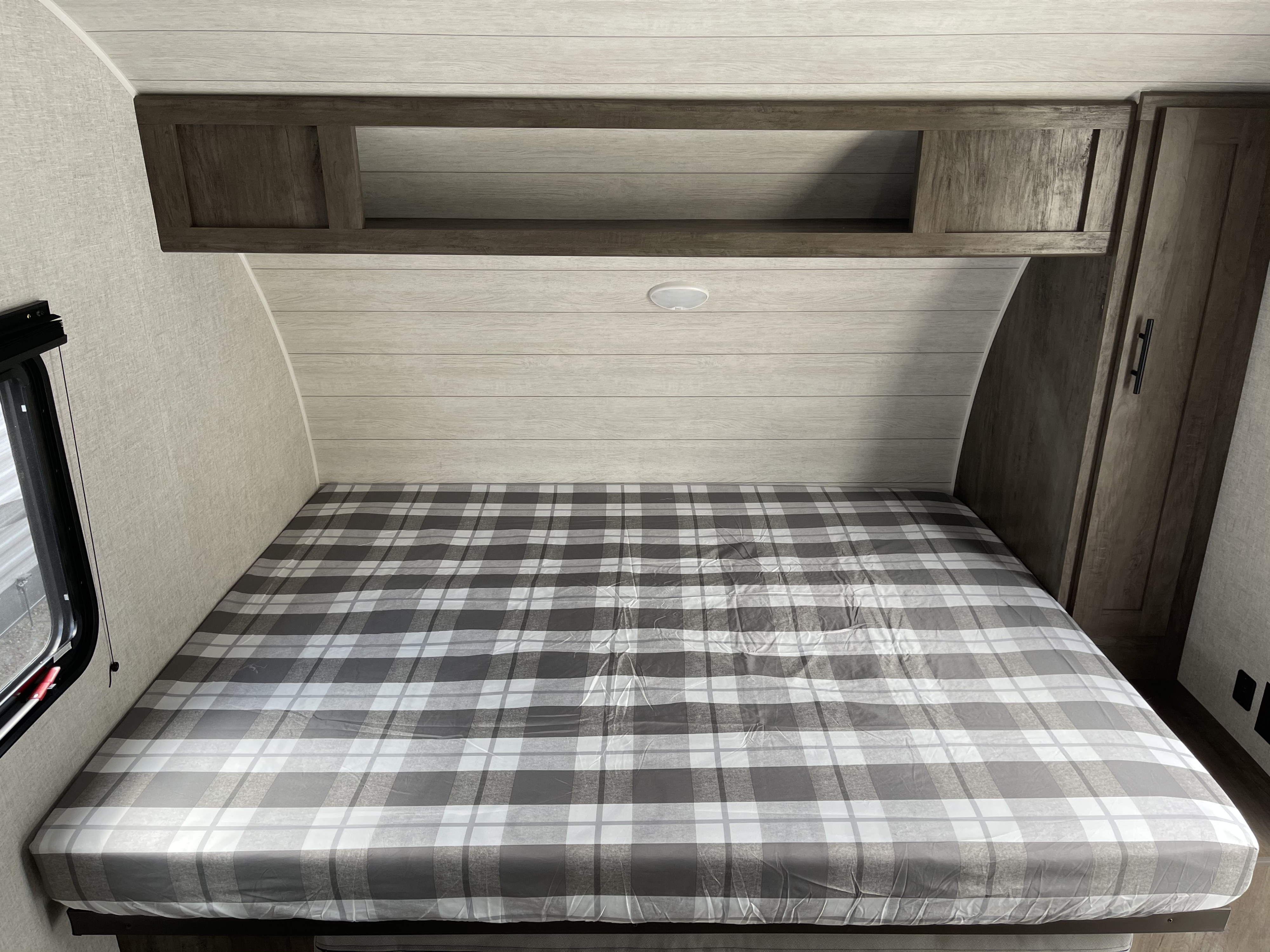 Comfortable RV rental bedroom featuring a plaid bed, overhead storage, and side wardrobe, perfect for your journey.. Forest River Salem 179 2021