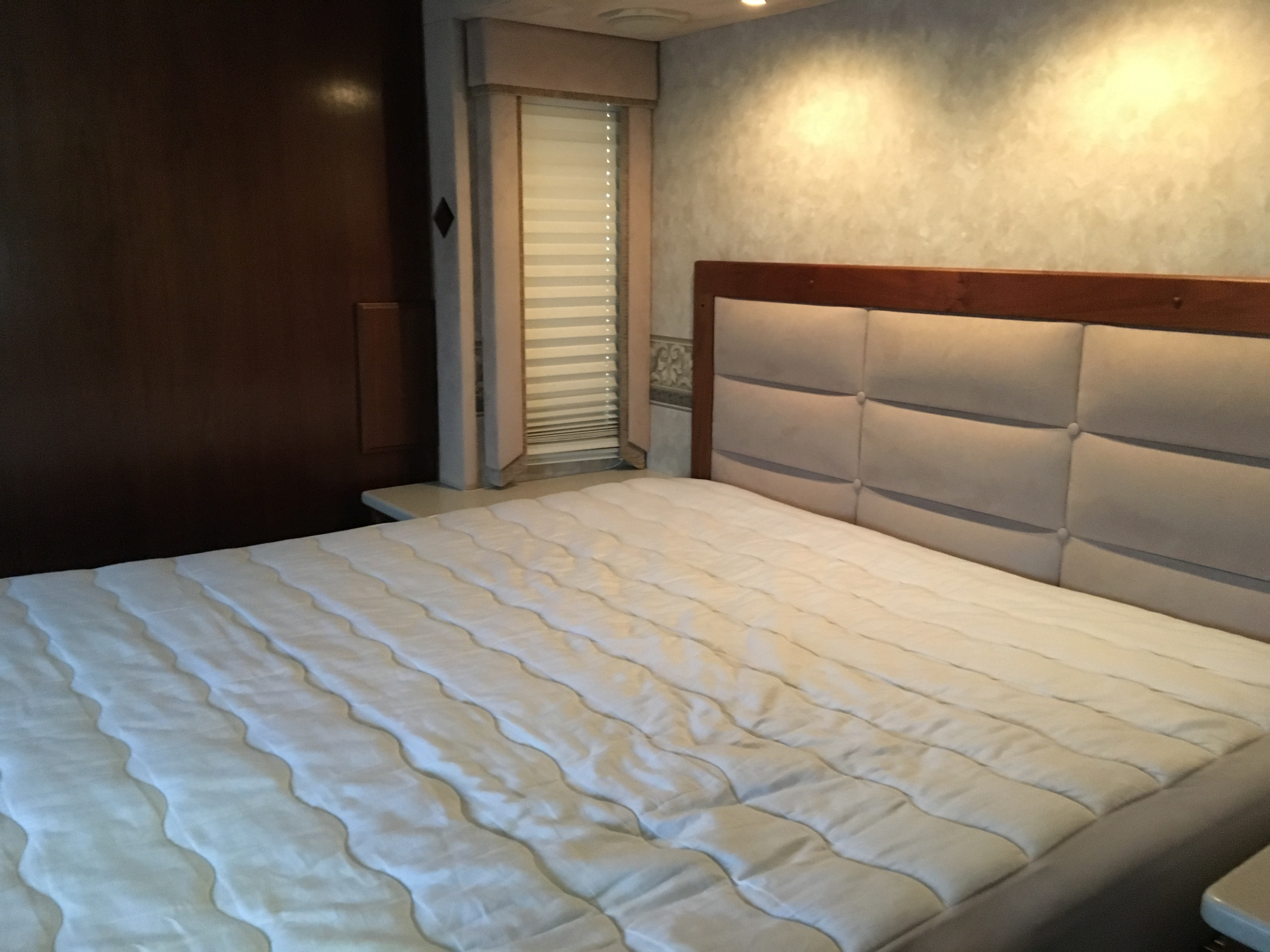 RV rental bedroom: a neatly made bed with white bedding, padded headboard, and a window with blinds.. Fleetwood Revolution Le 2005