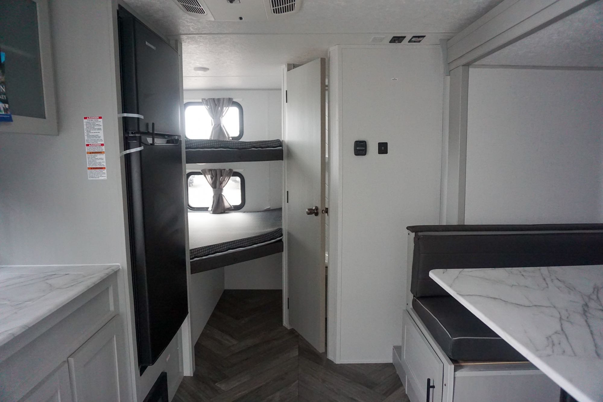 This modern rv rental interior features a black refrigerator, two bunk beds, and a cozy dinette with a marble-look table.. Forest River Wildwood 2021