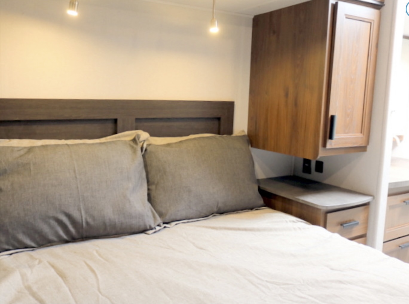 Comfortable RV rental bedroom featuring a full bed, built-in headboard, and wood storage cabinets with outlets.. Forest River Other 2021