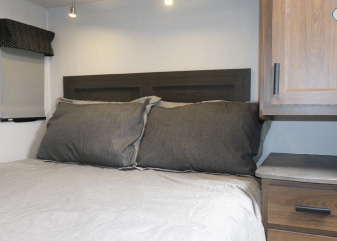 RV rental bedroom: a bed with a dark headboard, two grey pillows, light bedding, a window, and wood cabinets.. Forest River Other 2021