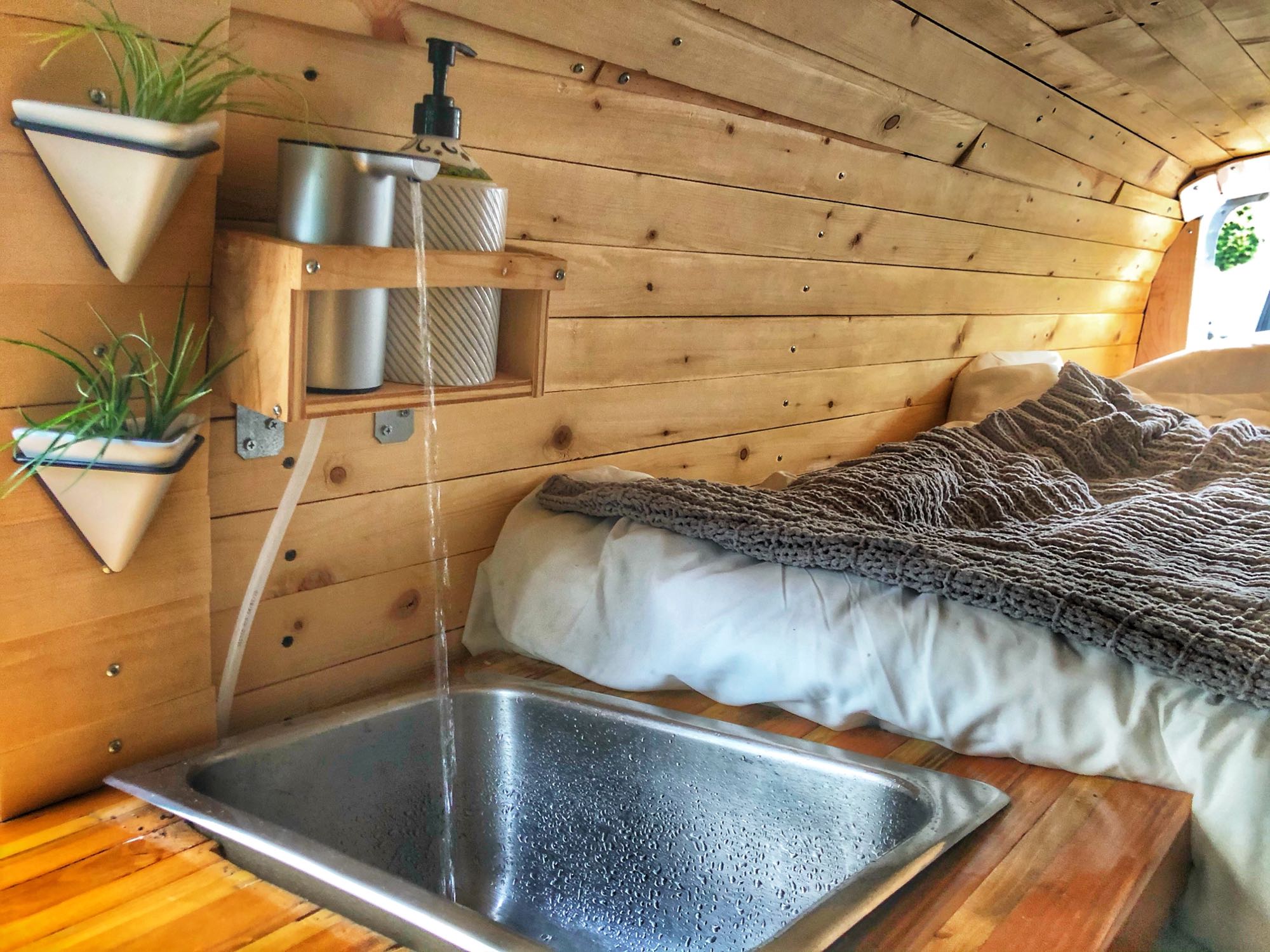 RV rental interior showing a compact bed, sink with running water, soap dispenser, and wall plants on wooden panels.. Ford Econoline E250supercab 2006