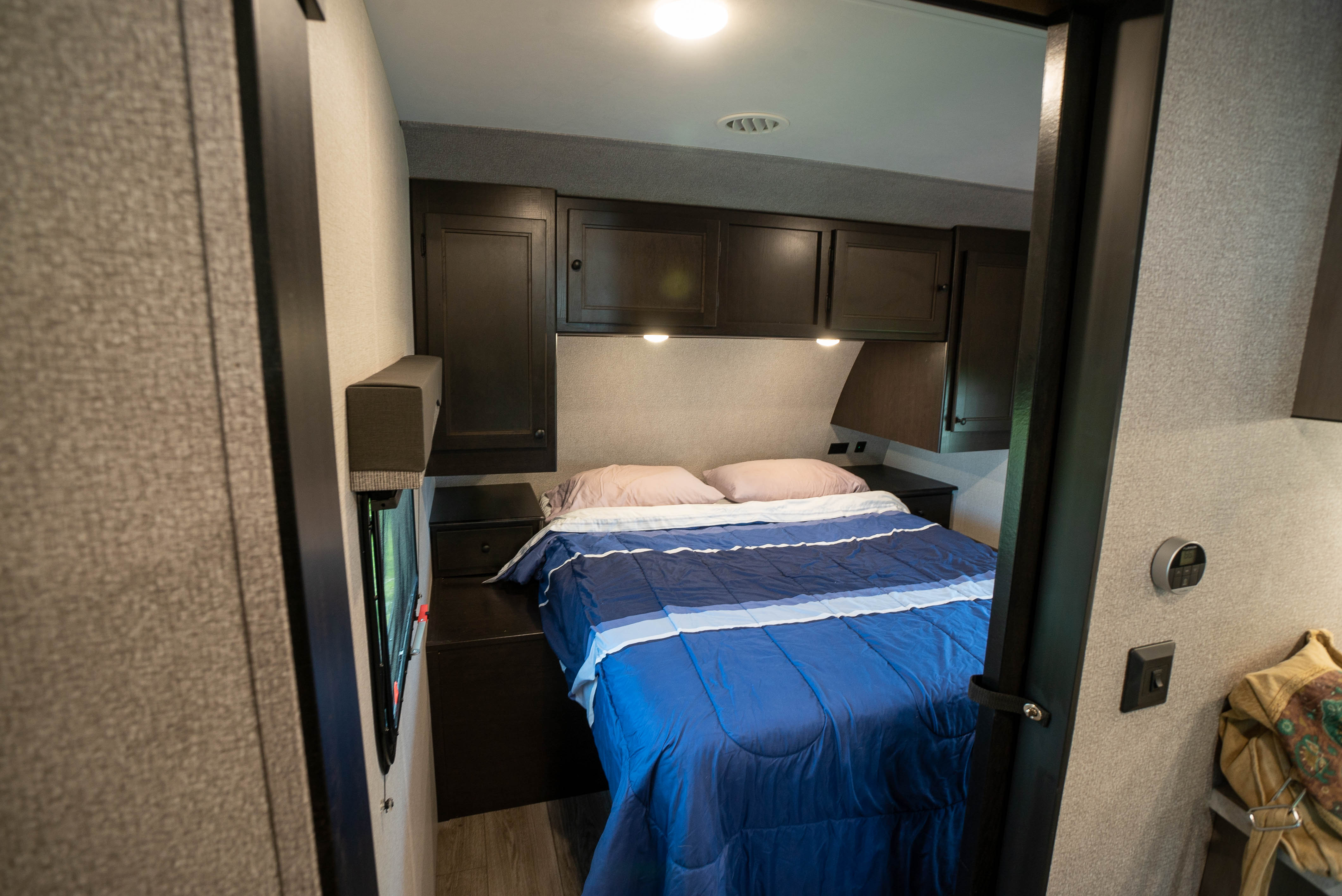 This cozy RV rental bedroom features dark wood cabinets, a blue bed, and modern controls for a comfy stay.. Starcraft Super Lite 2021