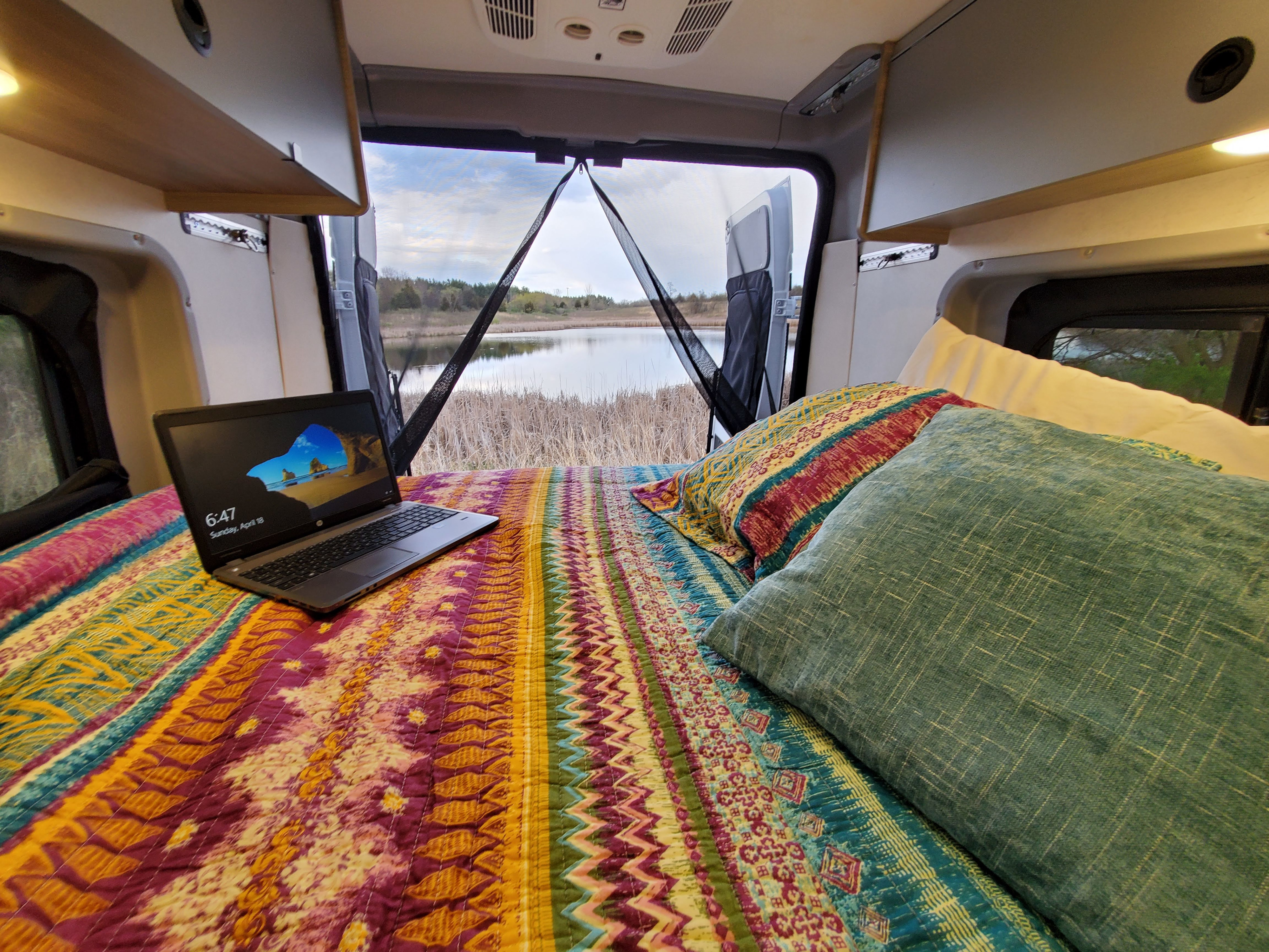 Cozy RV rental interior with bed, laptop, and scenic lake view. Perfect for remote work and travel.. Winnebago Solis 2022