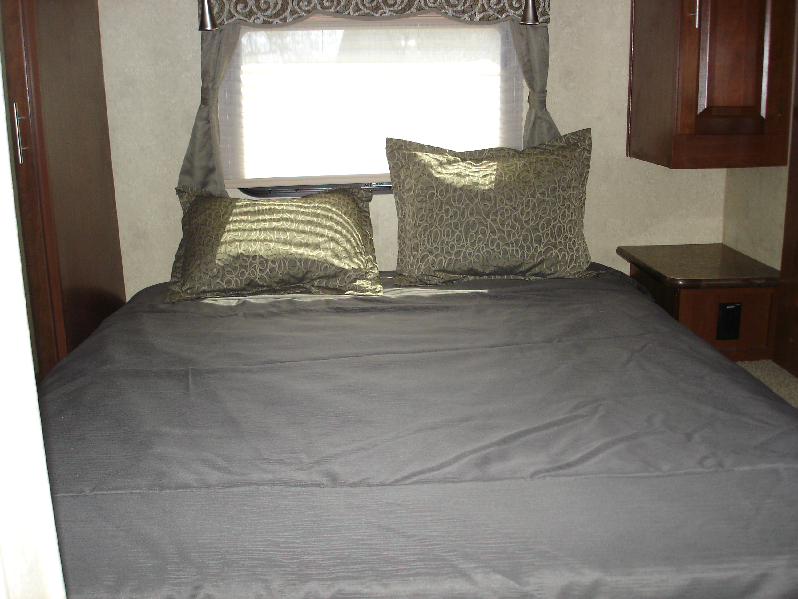 RV rental bedroom featuring a comfortable bed with dark gray bedding, decorative pillows, and a bright window above.. Flagstaff 26FKWS Super Lite 2016