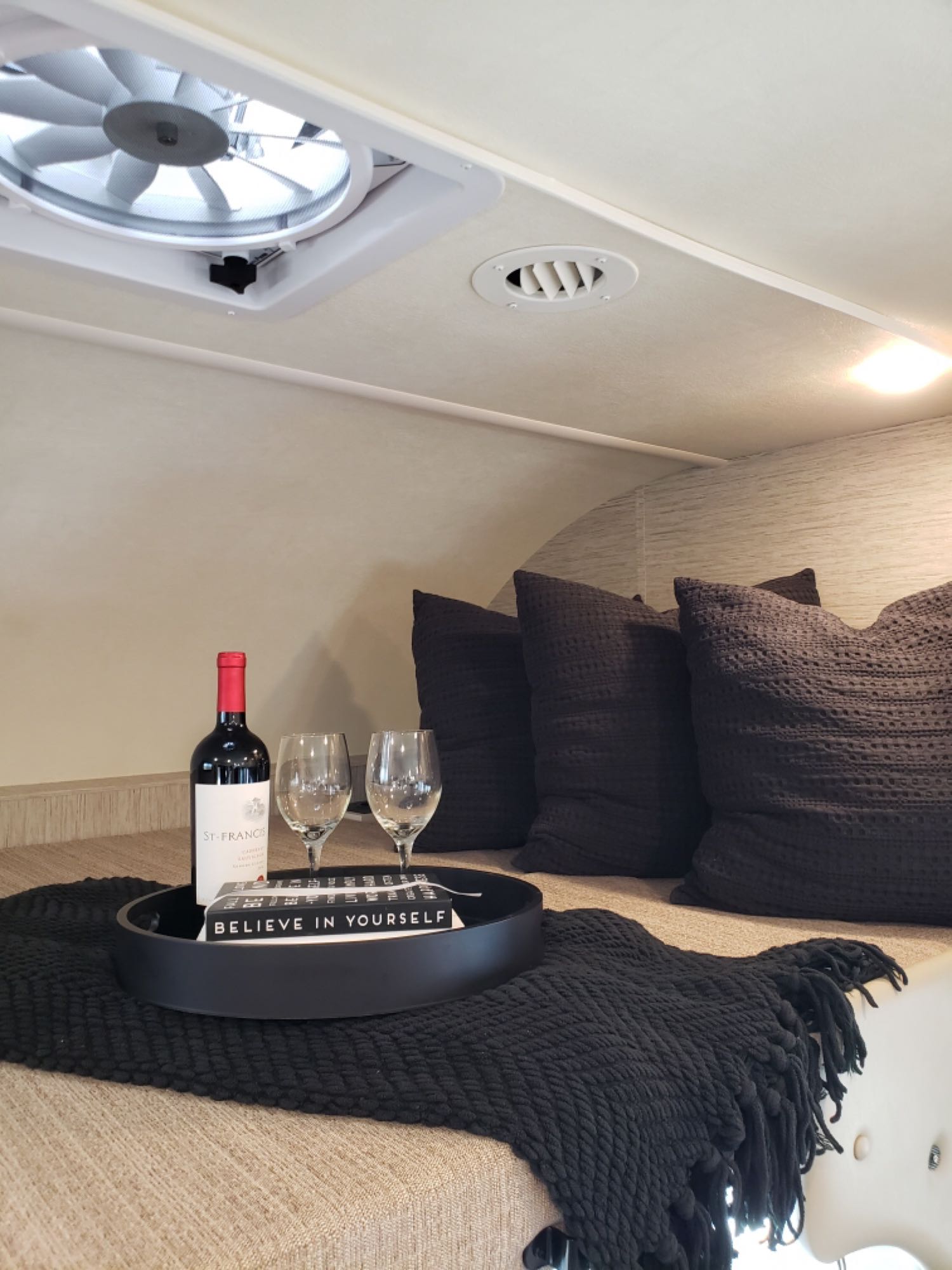 Enjoy a cozy RV rental night: wine, glasses, blanket, and soft pillows in a comfortable sleeping nook with a vent fan.. Thor Four Winds 2021