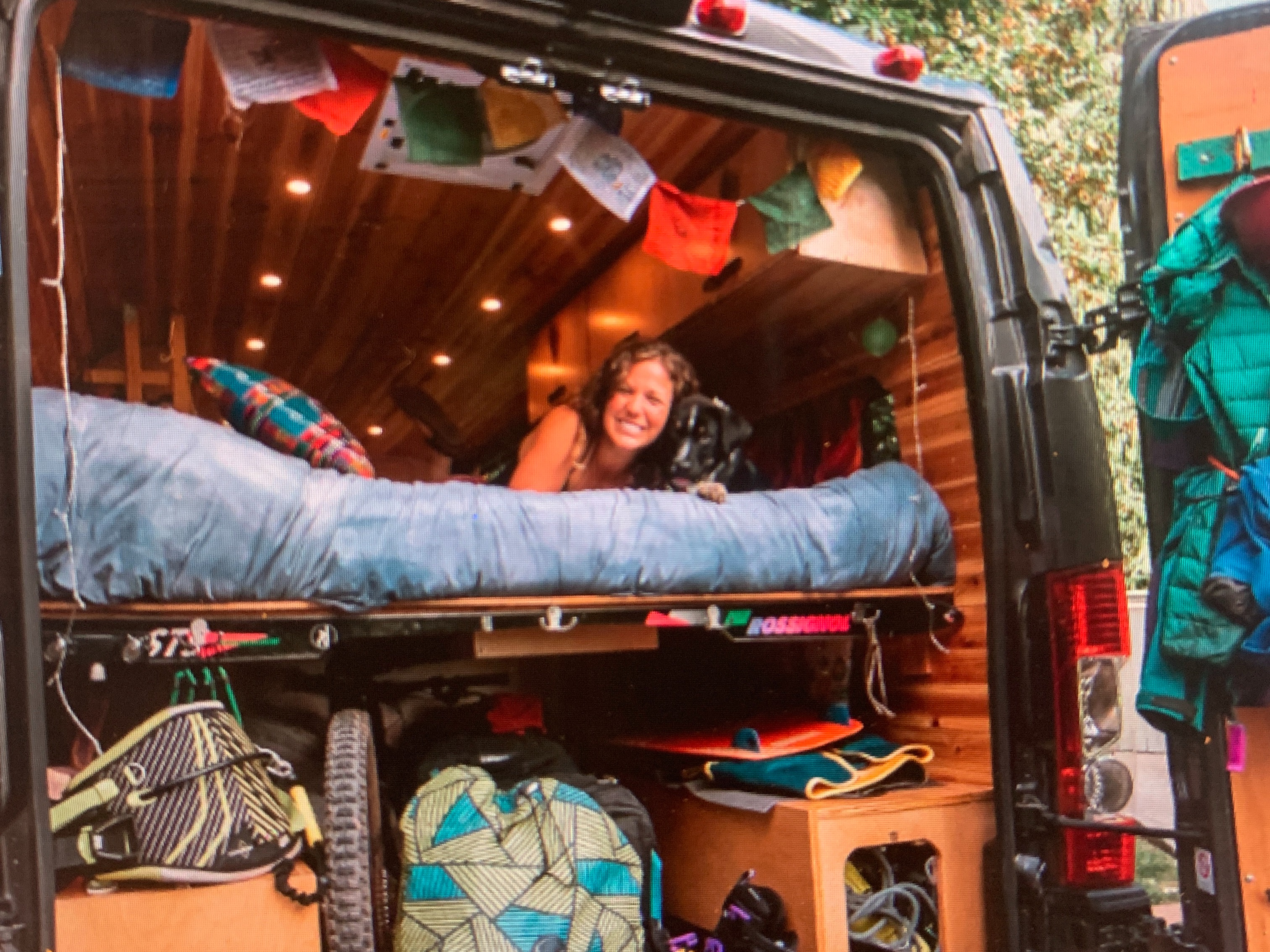 A comfortable RV rental interior, featuring a smiling traveler and dog on a bed in a wood-paneled camper van, equipped for adventures.. Dodge Sprinter Van 2019