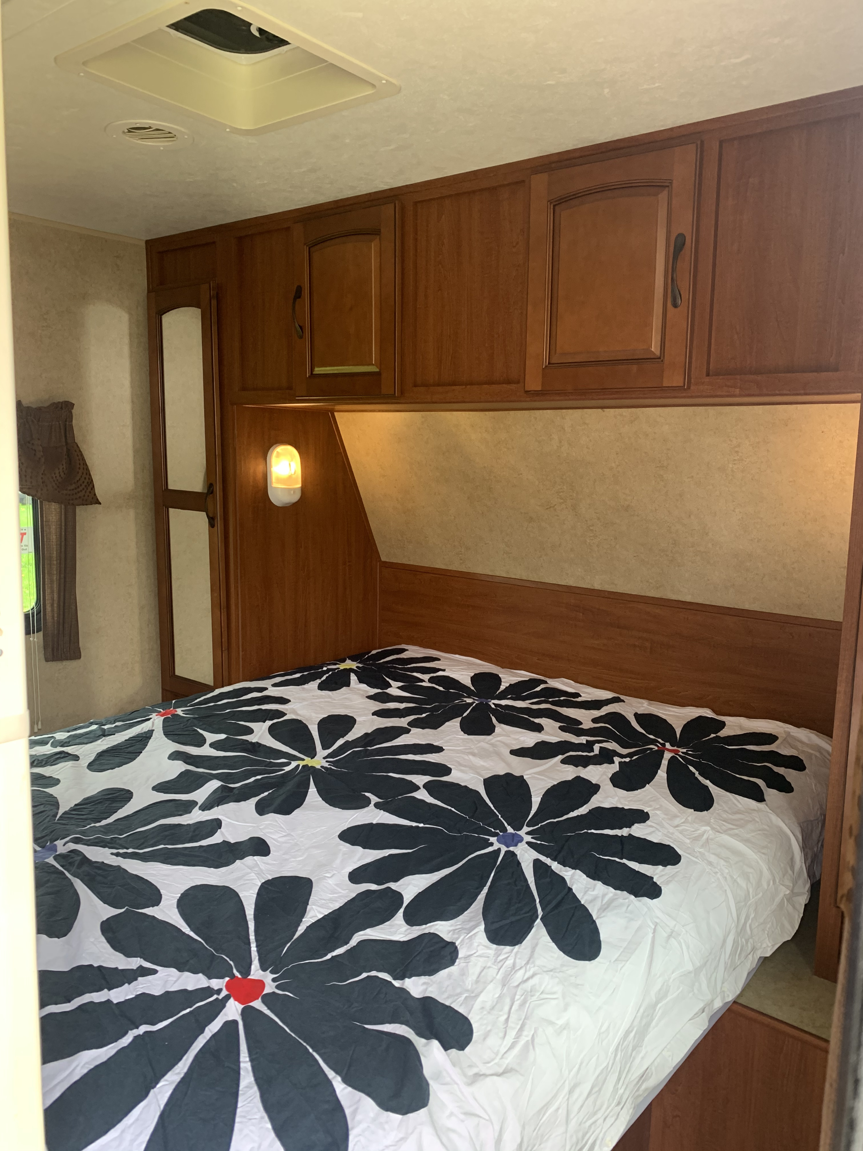Comfortable RV rental bedroom with a white duvet featuring bold black floral patterns & wooden storage.. Forest River Surveyor Sport 2014